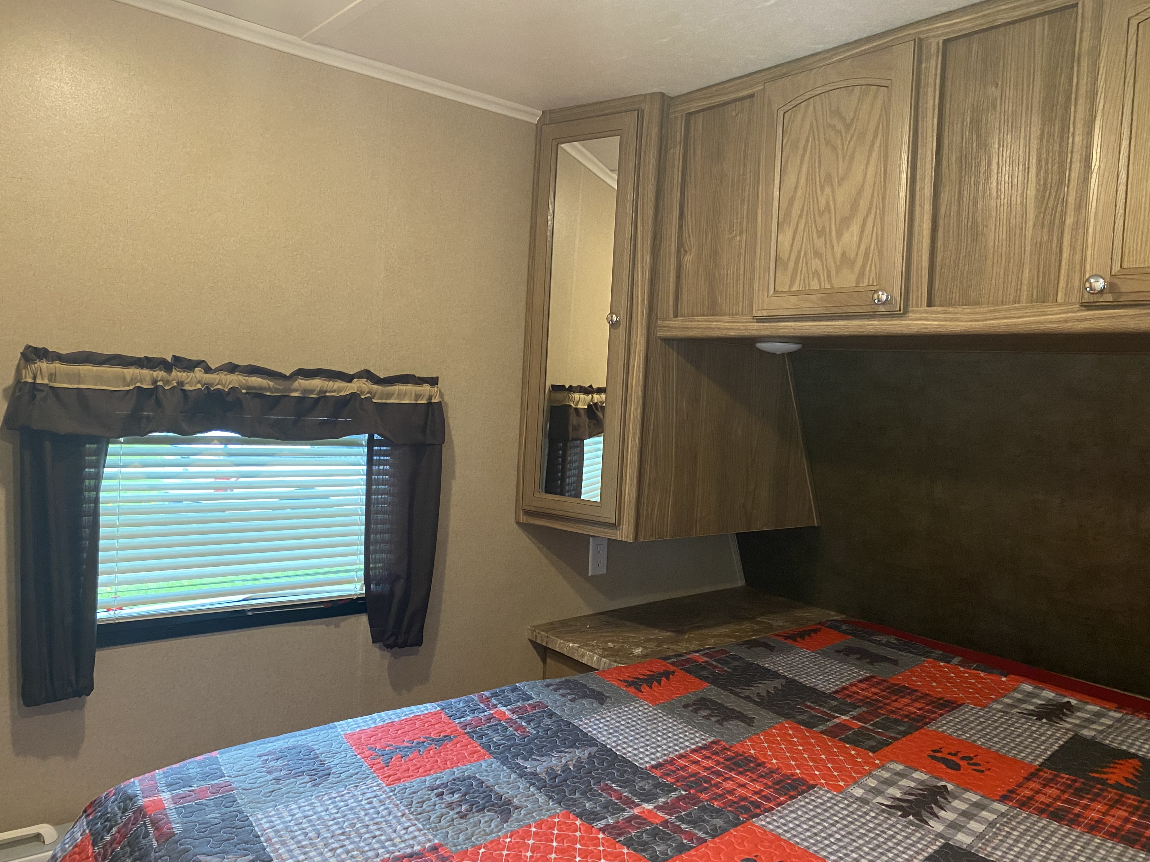 RV rental bedroom: window with blinds, wood cabinets (one mirrored), and a bed with a colorful patchwork quilt.. Forest River Shasta Revere 2016