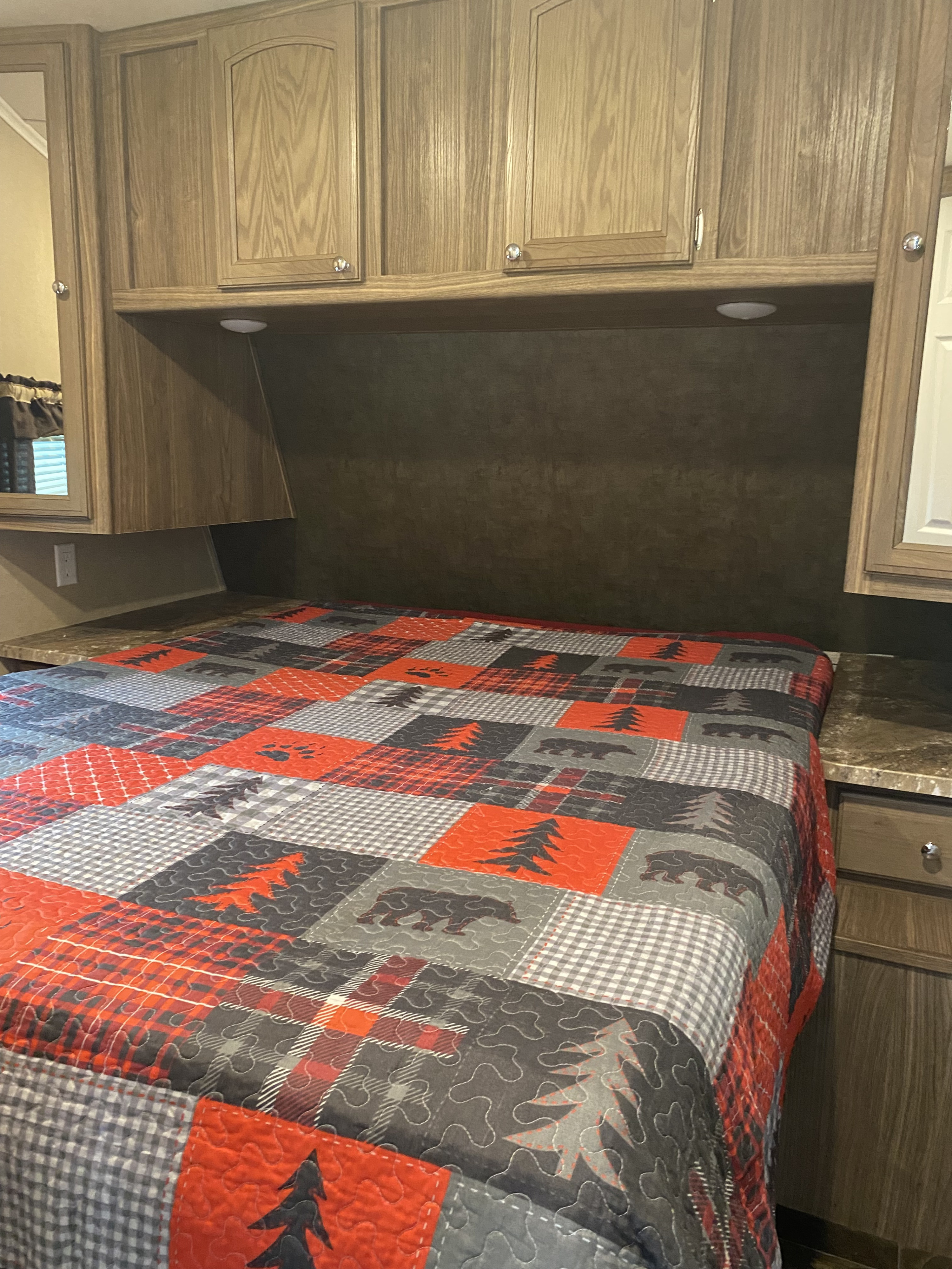 RV rental bedroom interior: a comfy bed with a bear/pine tree quilt, wood cabinets, and integrated lighting for cozy nights.. Forest River Shasta Revere 2016