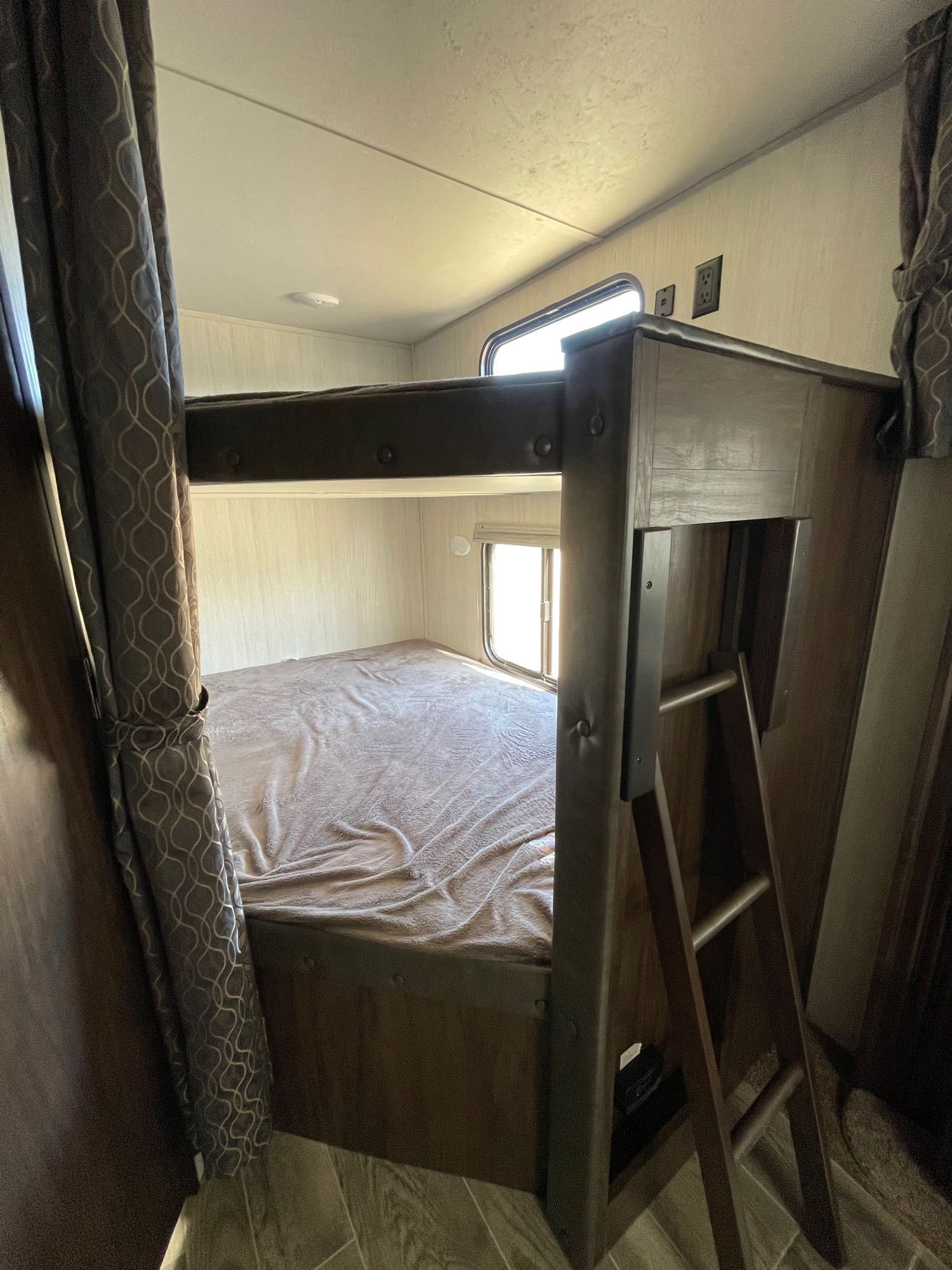 Inside an RV rental: a cozy lower bed, upper bunk with ladder, windows, & patterned curtains.. Forest River Cherokee 2019