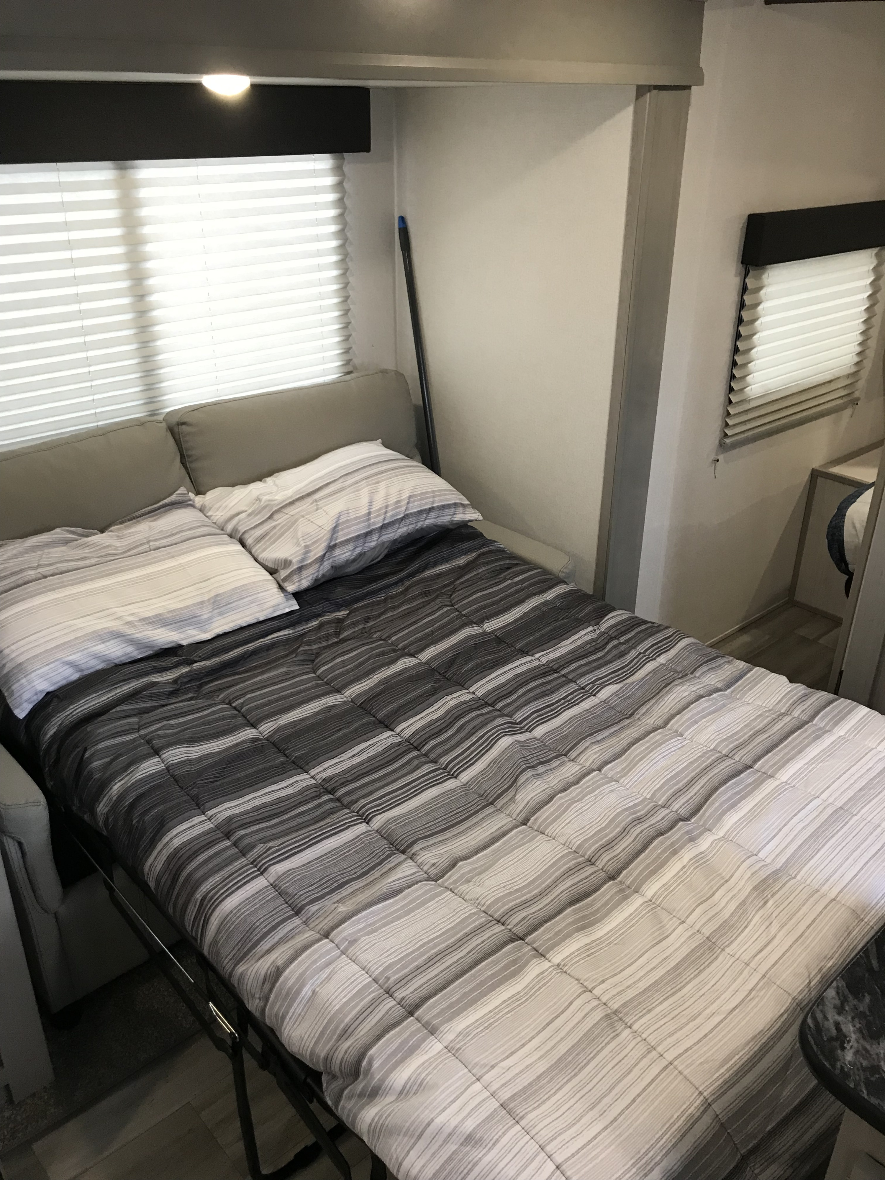 Interior of an RV rental featuring a striped comforter on a fold-out bed with pillows, next to windows with blinds.. Forest River Tracer LE 2022