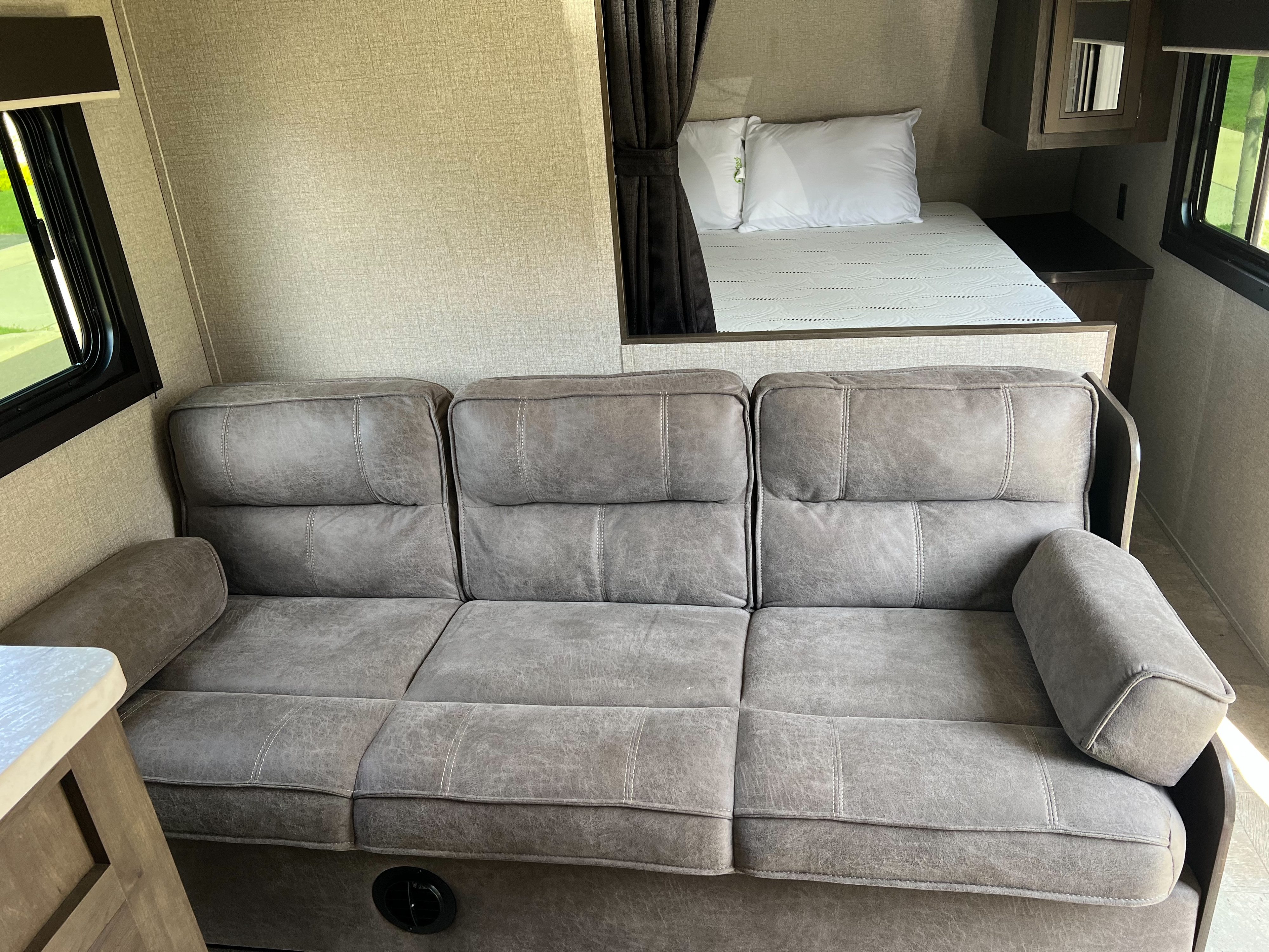 RV rental interior showcases a comfy grey sofa and a raised bed nook, perfect for relaxing in this modern camper.. Jayco Jay Flight SLX 2020