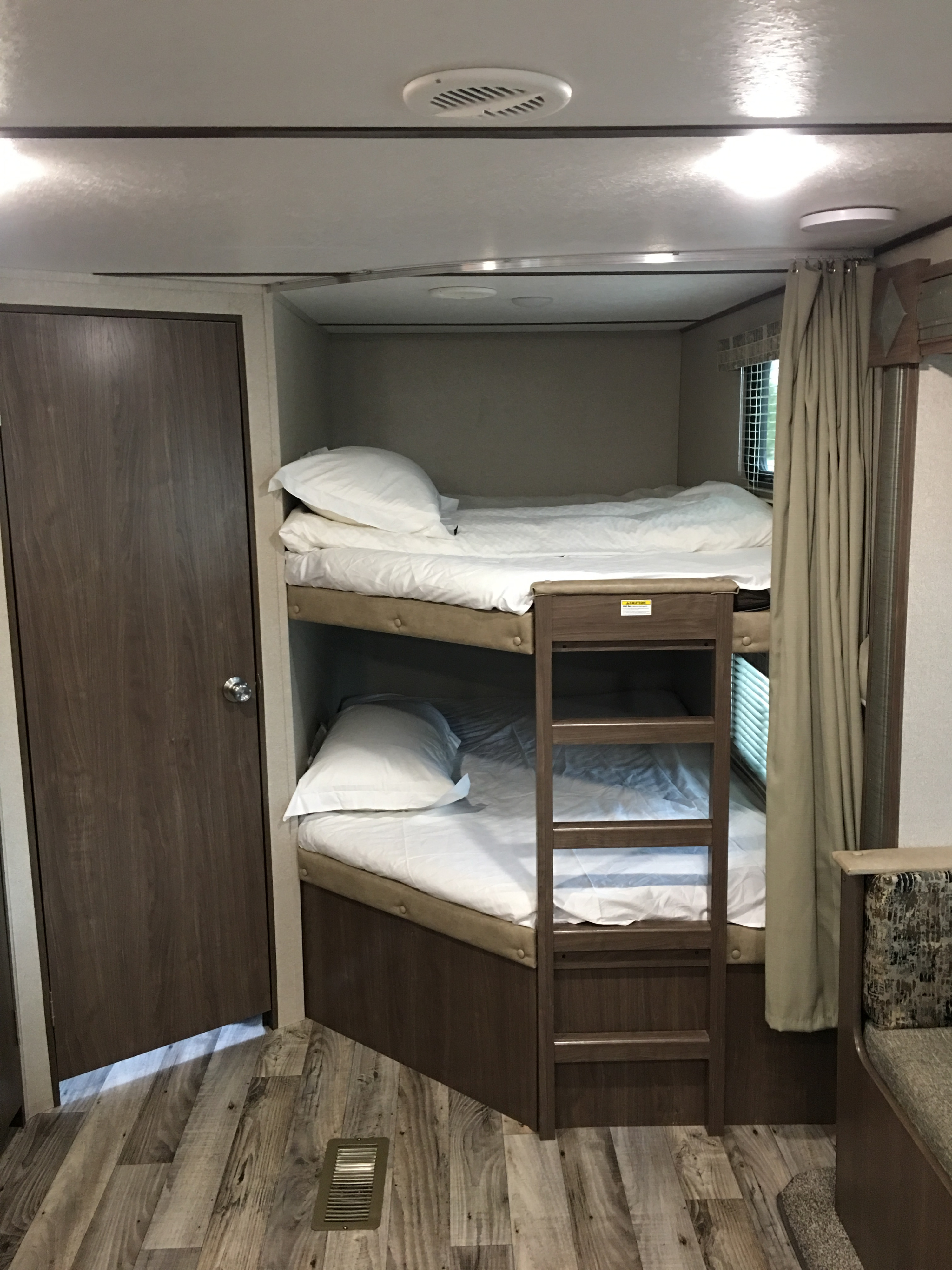 Inside an RV rental: a neat bunk bed setup with white bedding, wooden ladder, and a nearby door, offering comfortable sleeping quarters.. Keystone RV Hideout LHS 2019