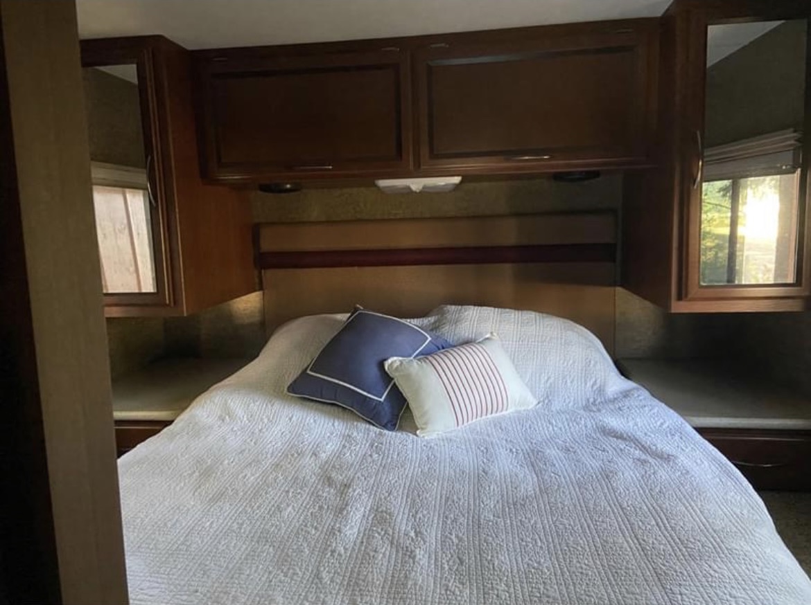 Cozy RV rental bedroom featuring a comfortable queen bed with white bedding, pillows, overhead cabinets, and windows.. A.C.E. A.C.E. Motorhome 2013