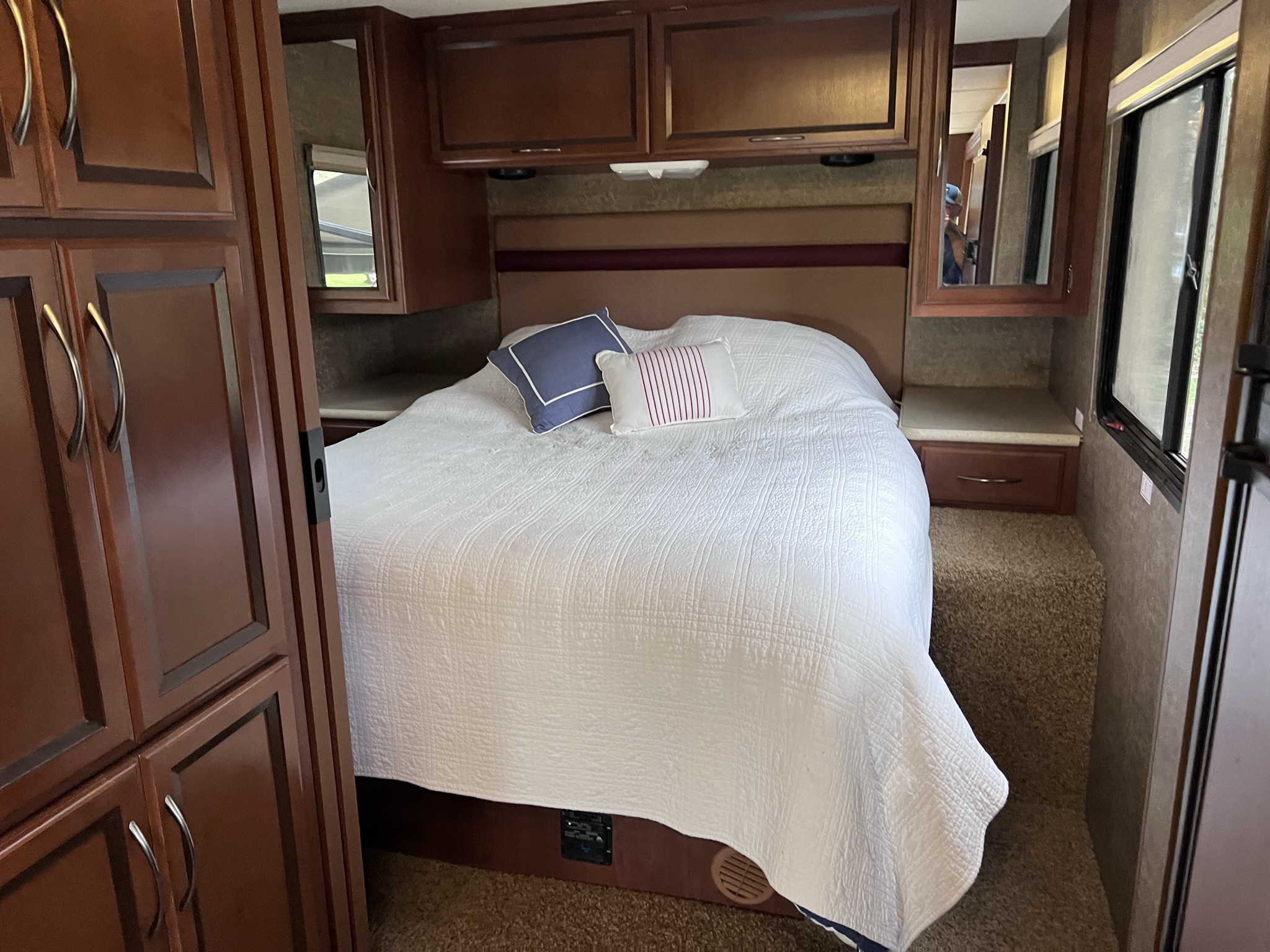 This RV rental offers a cozy bedroom: a bed with white bedding, pillows, wooden cabinets, and a window for comfortable travels.. A.C.E. A.C.E. Motorhome 2013