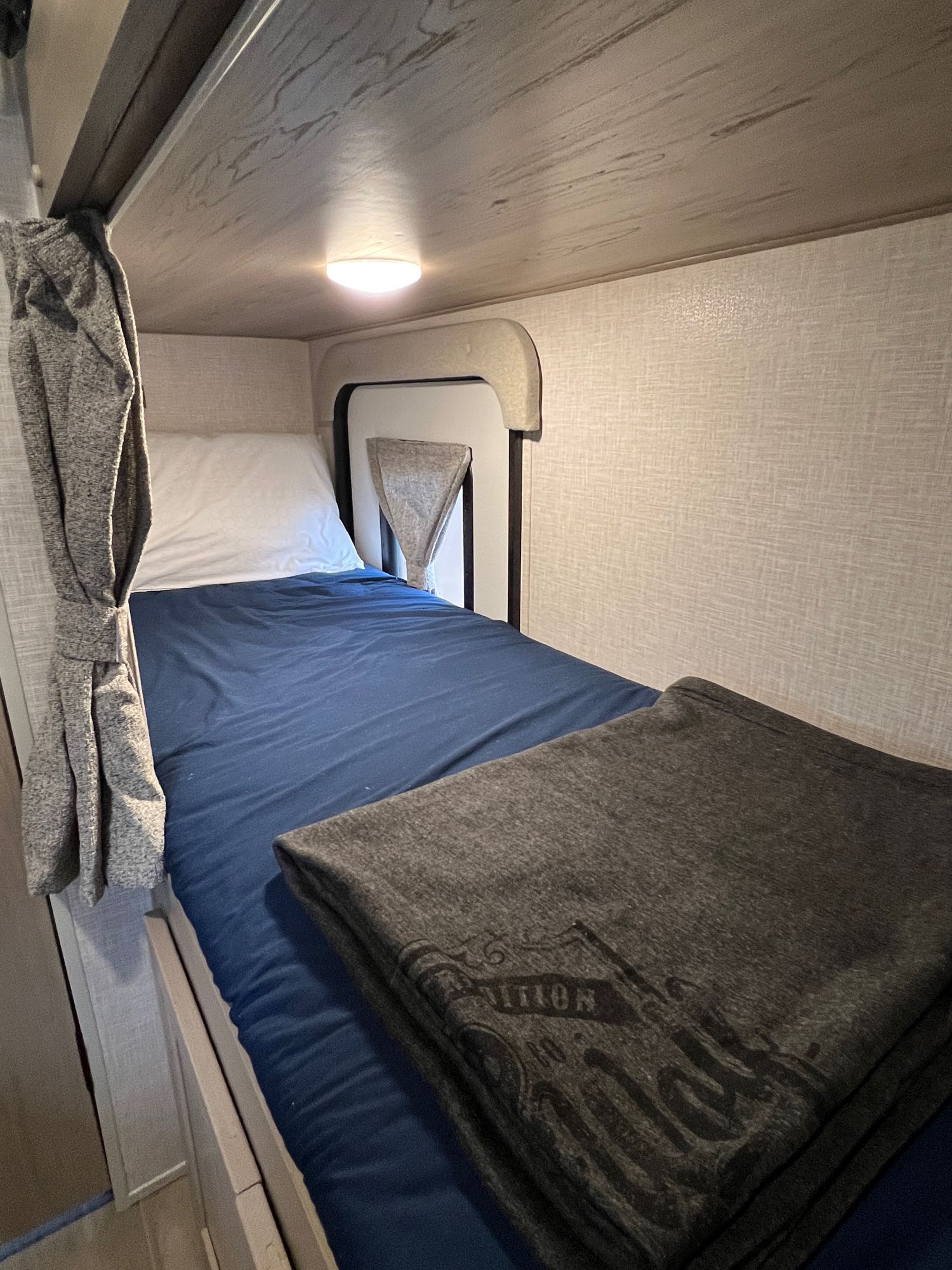 Cozy RV rental bunk bed with blue sheets, white pillow, and a folded grey blanket, perfect for travelers.. Forest River Flagstaff E-Pro 2023