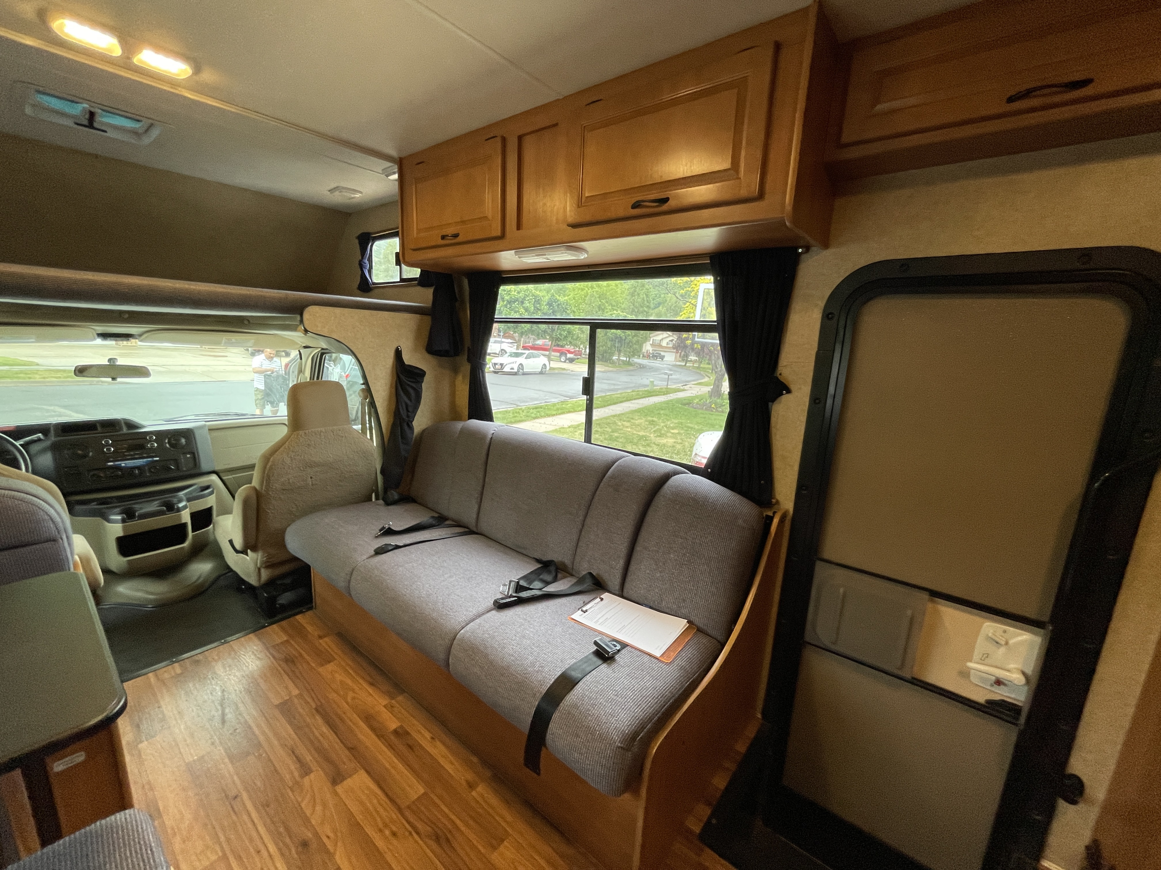 Spacious RV rental interior: View of the main living area with a comfy gray couch, wood floor, overhead storage, and driver's cabin.. Majestic Leisure Craft Tourer Ii 2015