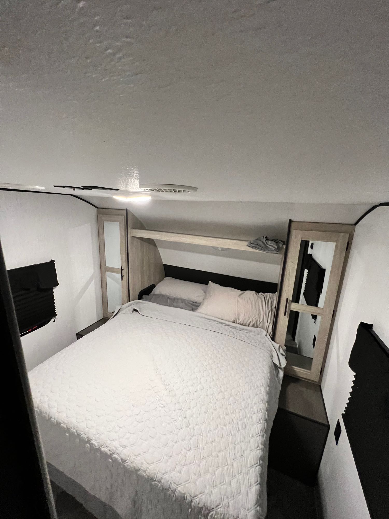 Cozy RV rental bedroom featuring a large bed with white bedding, dual wardrobes, overhead shelf, and black window blinds.. Heartland RVs Prowler 2022