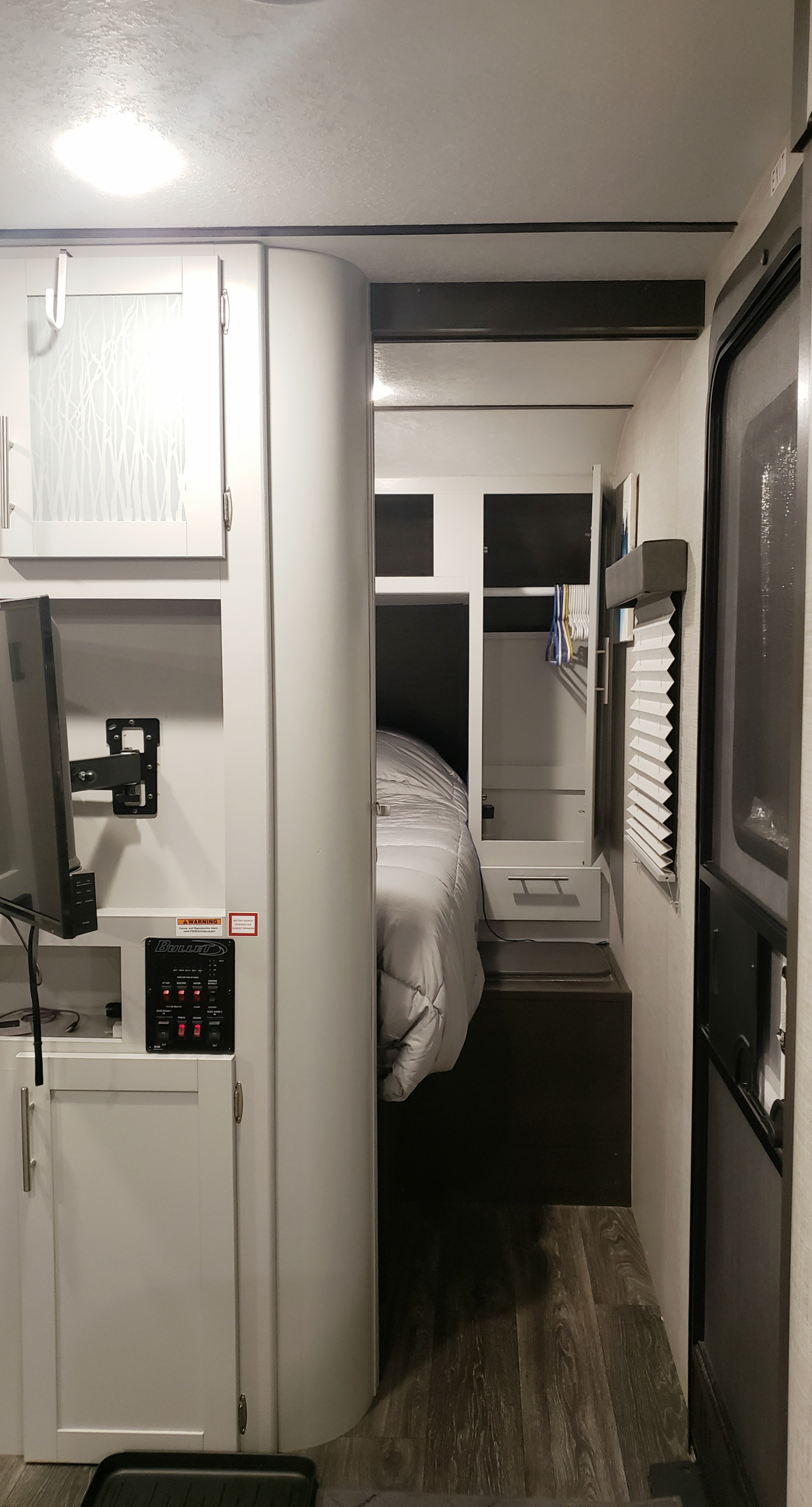 Modern RV rental interior, showing a living area with TV and control panel, leading to a cozy bedroom.. Keystone RV Bullet Ultra Lite 2020
