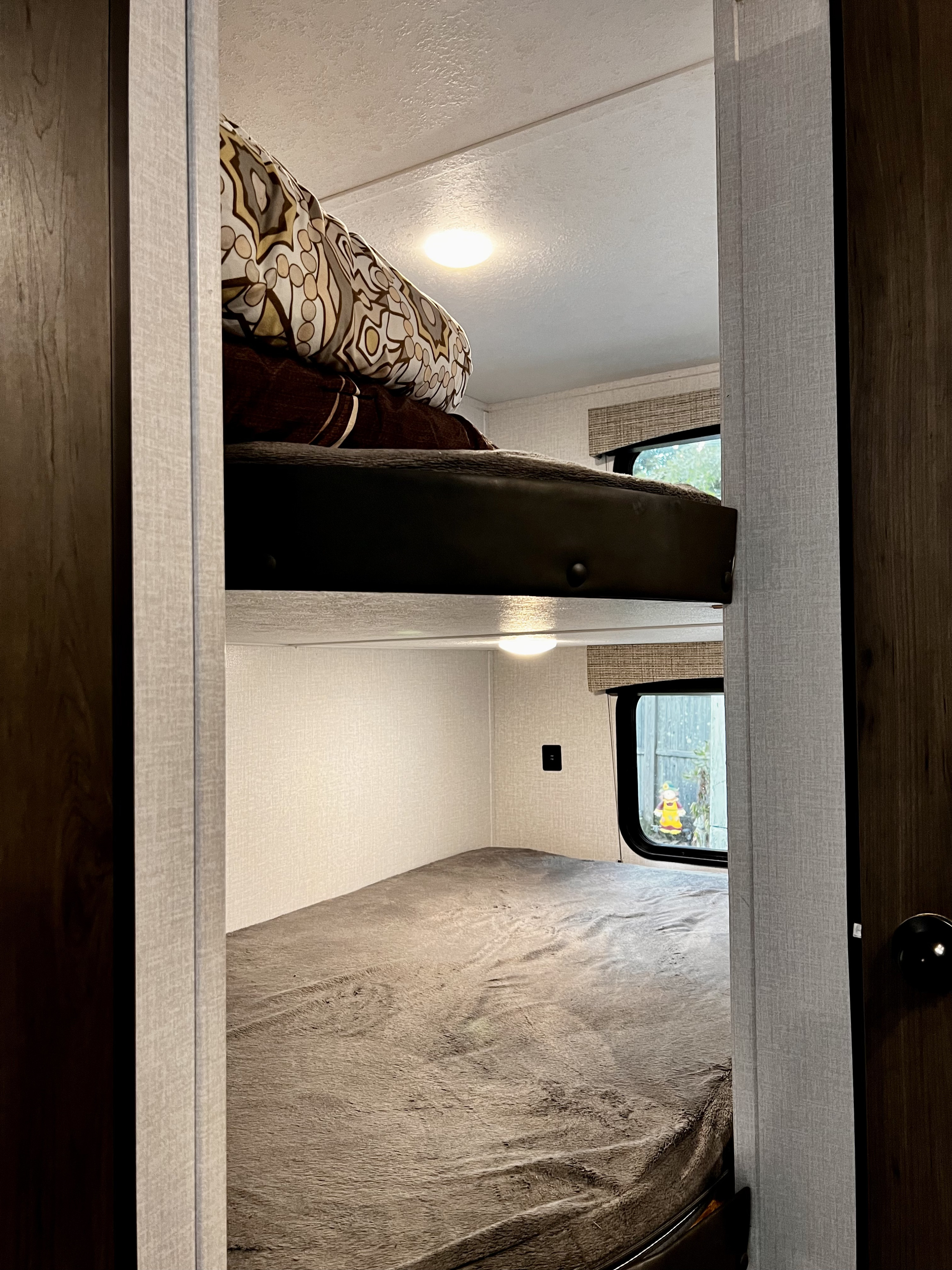 This RV rental interior features two bunk beds, with a patterned comforter on the upper bunk and a grey blanket on the lower, near a window.. Independence Trail 188DBK 2022