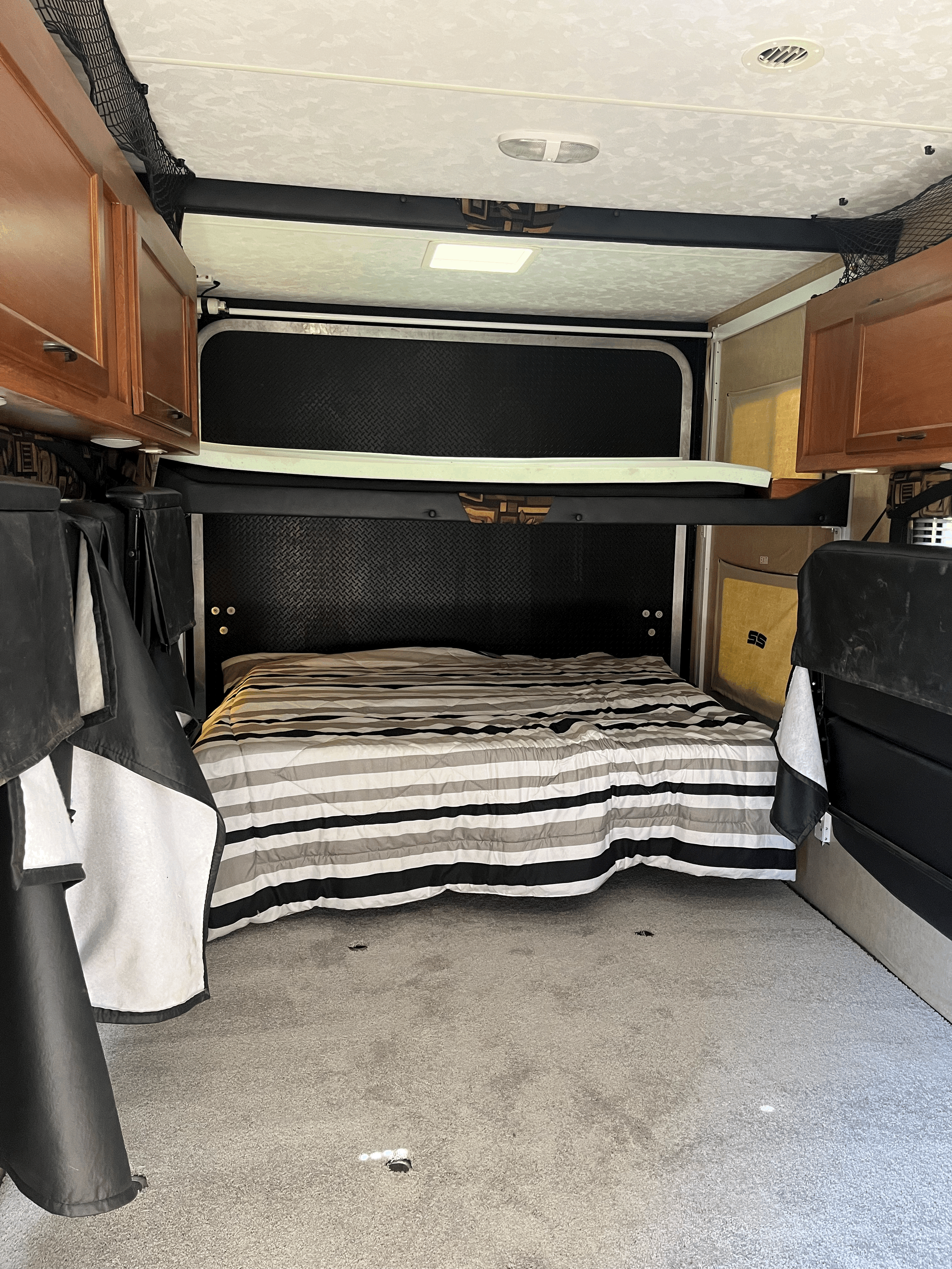 Spacious RV rental bedroom featuring a comfy striped bed, carpeted floor, and an overhead bunk.. Pacific Coachworks Sandsport 2013