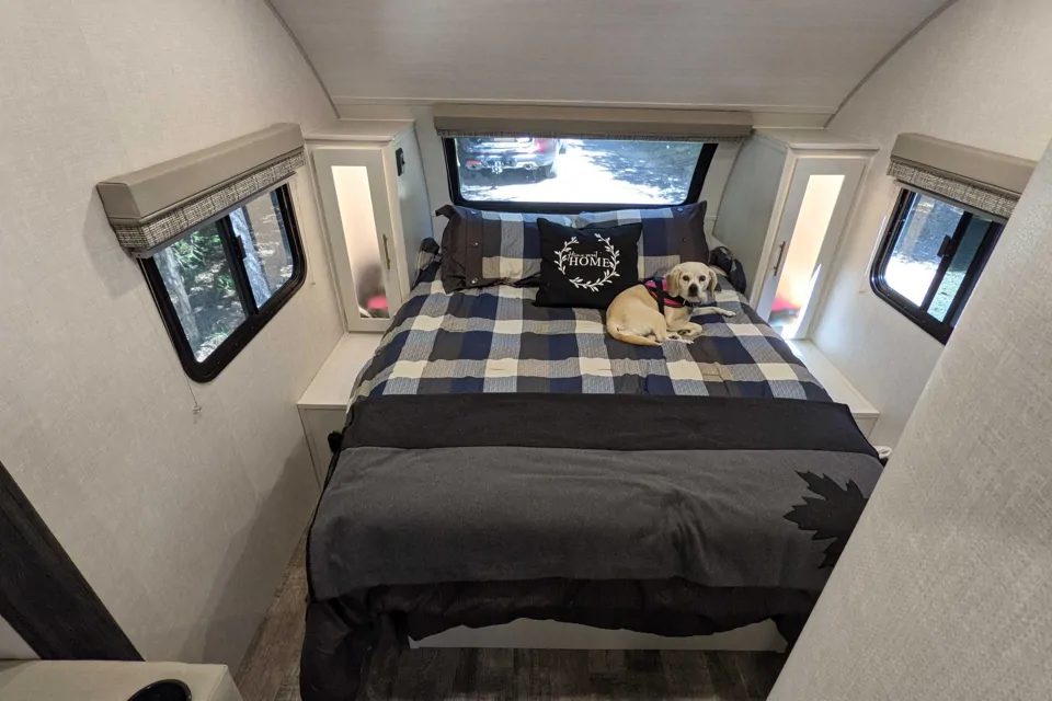 Cozy RV rental bedroom with a cute dog on a plaid bed, featuring a "HOME" pillow and large windows.. R-Pod R-Pod Trailer 2022