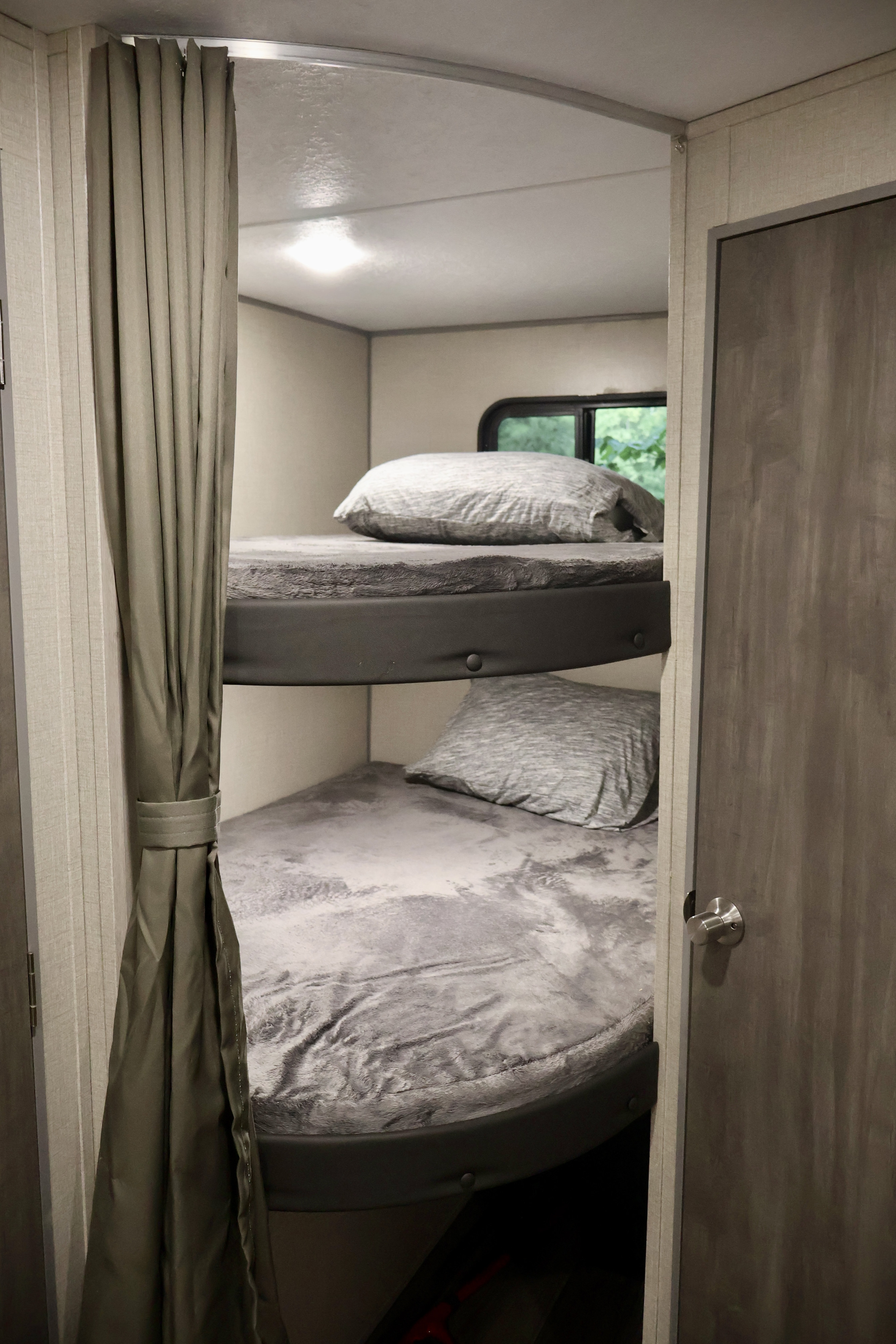 Cozy bunk beds in an RV rental, featuring grey bedding, pillows, and a window view, creating a comfortable sleeping area.. Coachmen Other 2023