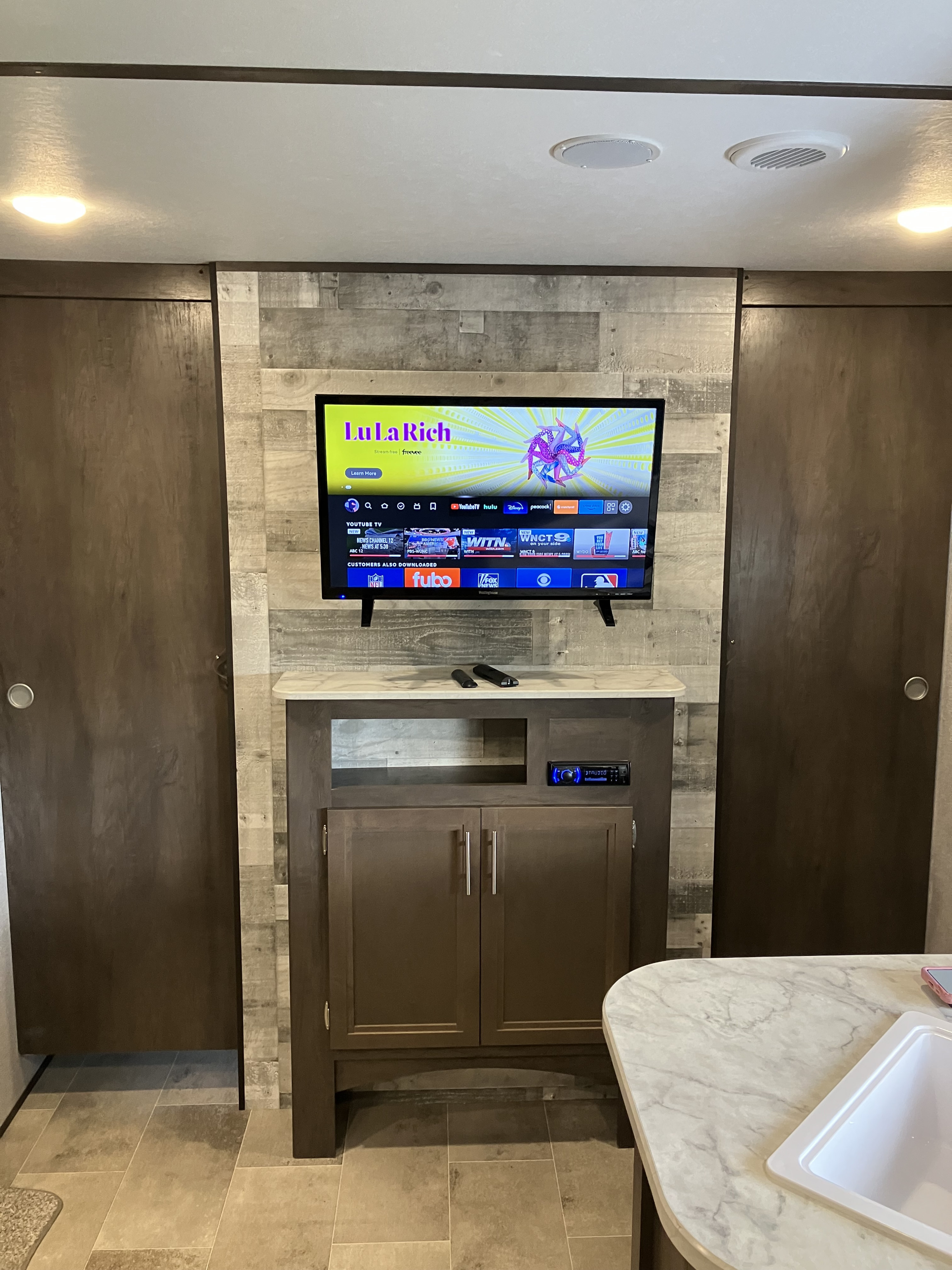 Modern RV rental interior with an entertainment center: smart TV showing streaming apps and built-in audio.. Dutchmen Coleman Lantern LT 2021