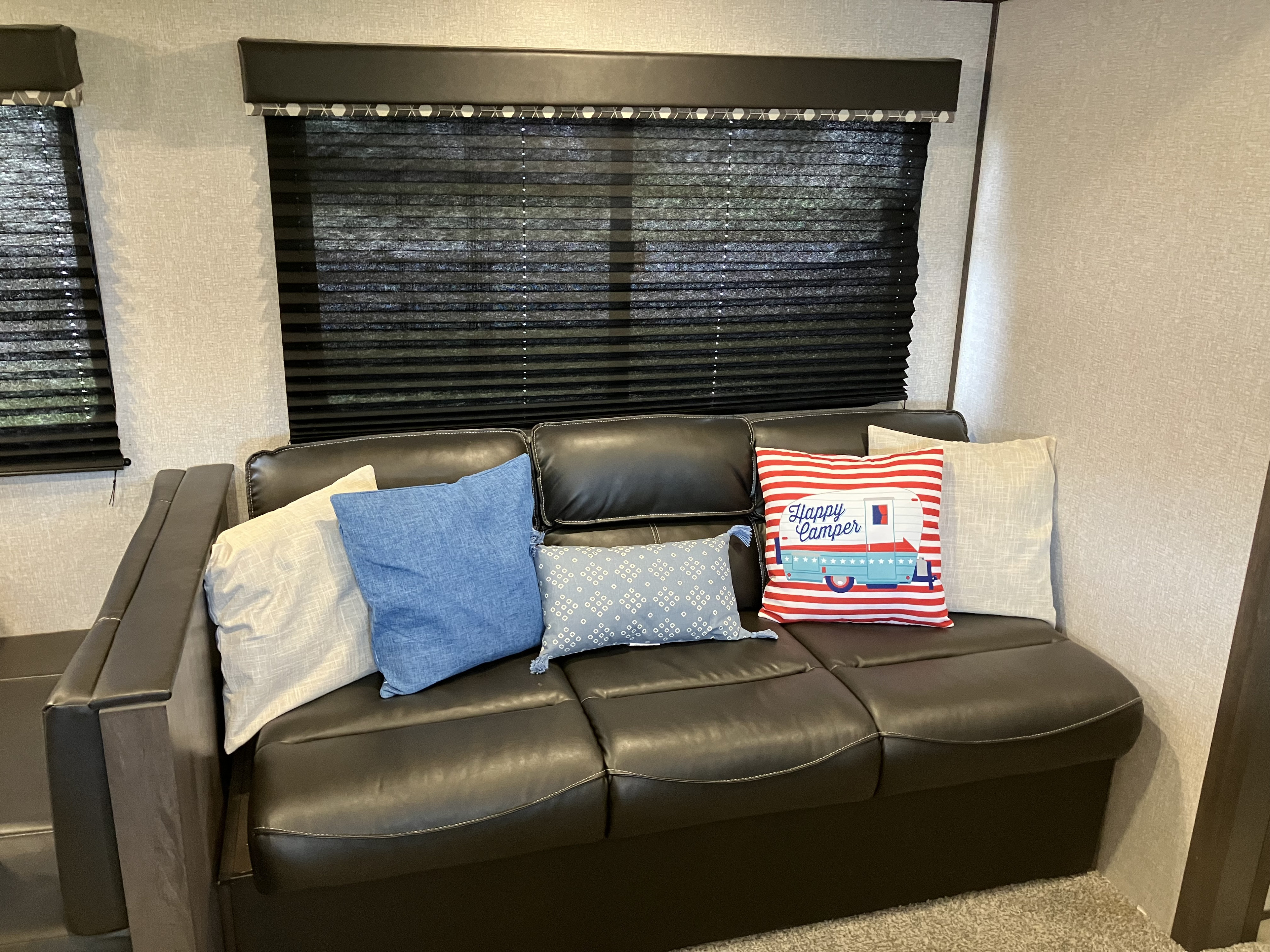 RV rental: a cozy dark sofa with assorted pillows, including a "Happy Camper" design, and pulled-down window blinds.. Dutchmen Coleman Lantern LT 2021