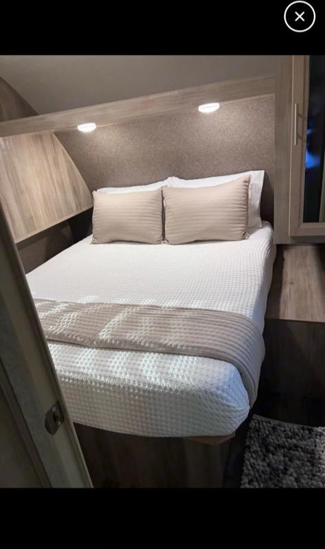 Cozy RV rental bedroom featuring a comfortable bed with textured white bedding, light pillows, and overhead reading lights.. Coachmen Forest River Catalina 2019