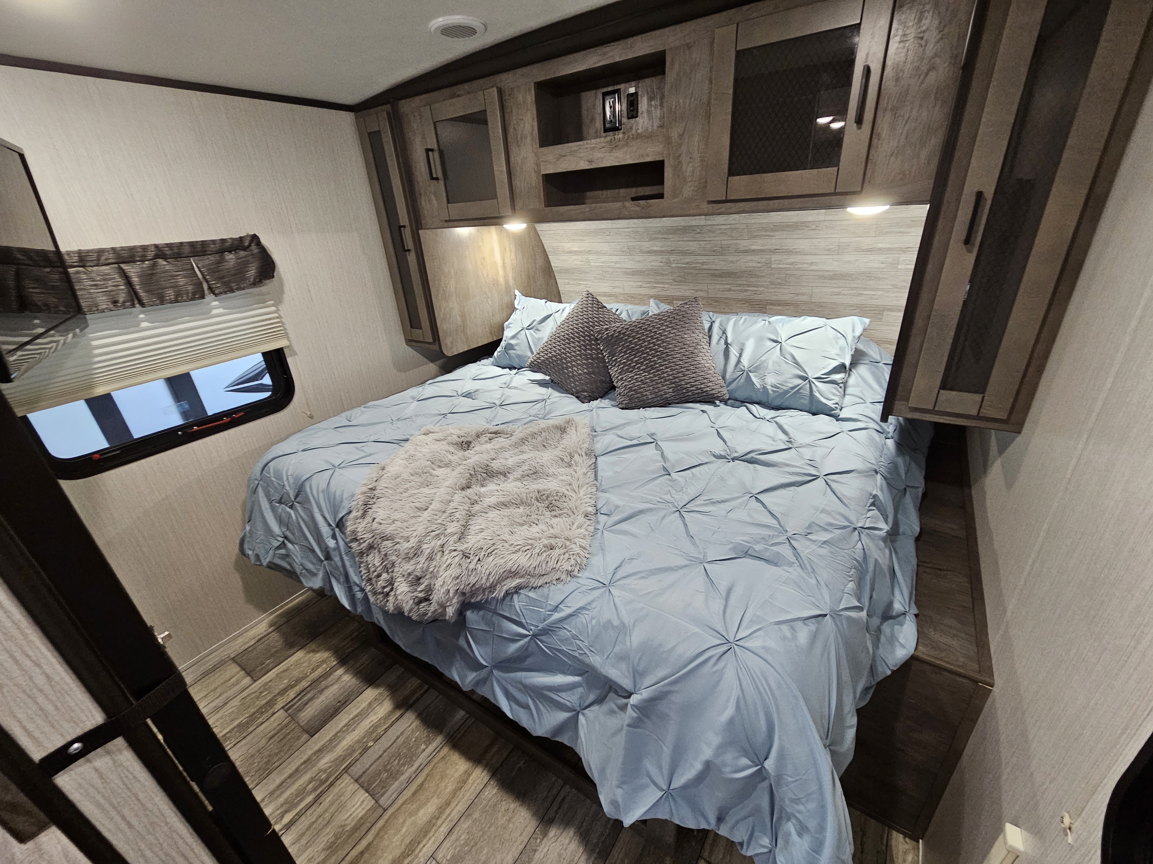 Cozy RV rental bedroom showcasing a bed with blue comforter, accent pillows, and modern overhead cabinets.. Heartland RVs North Trail 2020