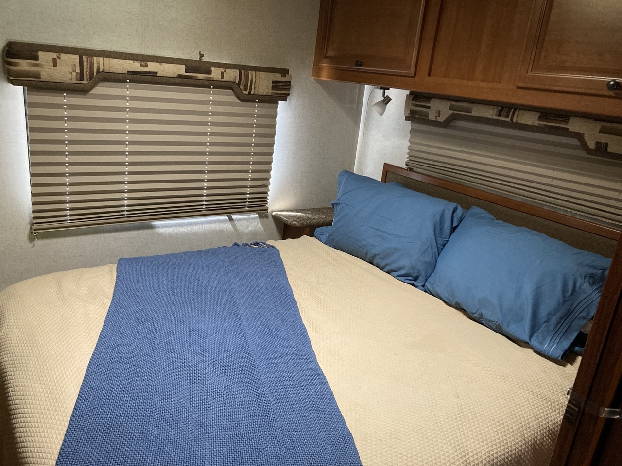 Inside an RV rental: a compact bedroom with a bed, blue pillows, and a textured blanket under practical window blinds.. Jamboree Jamboree Motorhome 2011