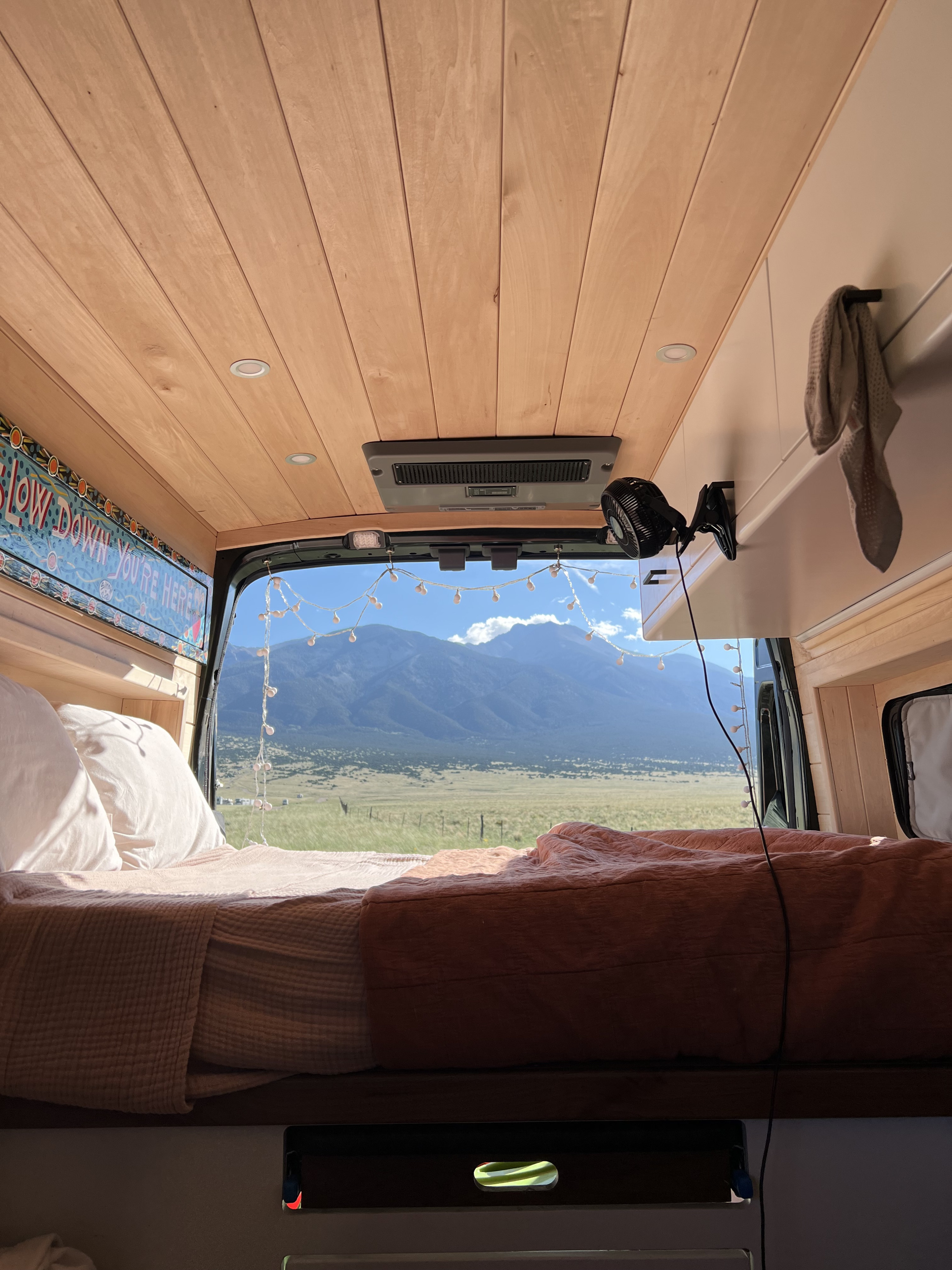 Enjoy breathtaking mountain views from your cozy RV rental bed, featuring string lights and a wooden interior.. Ford Transit 2020