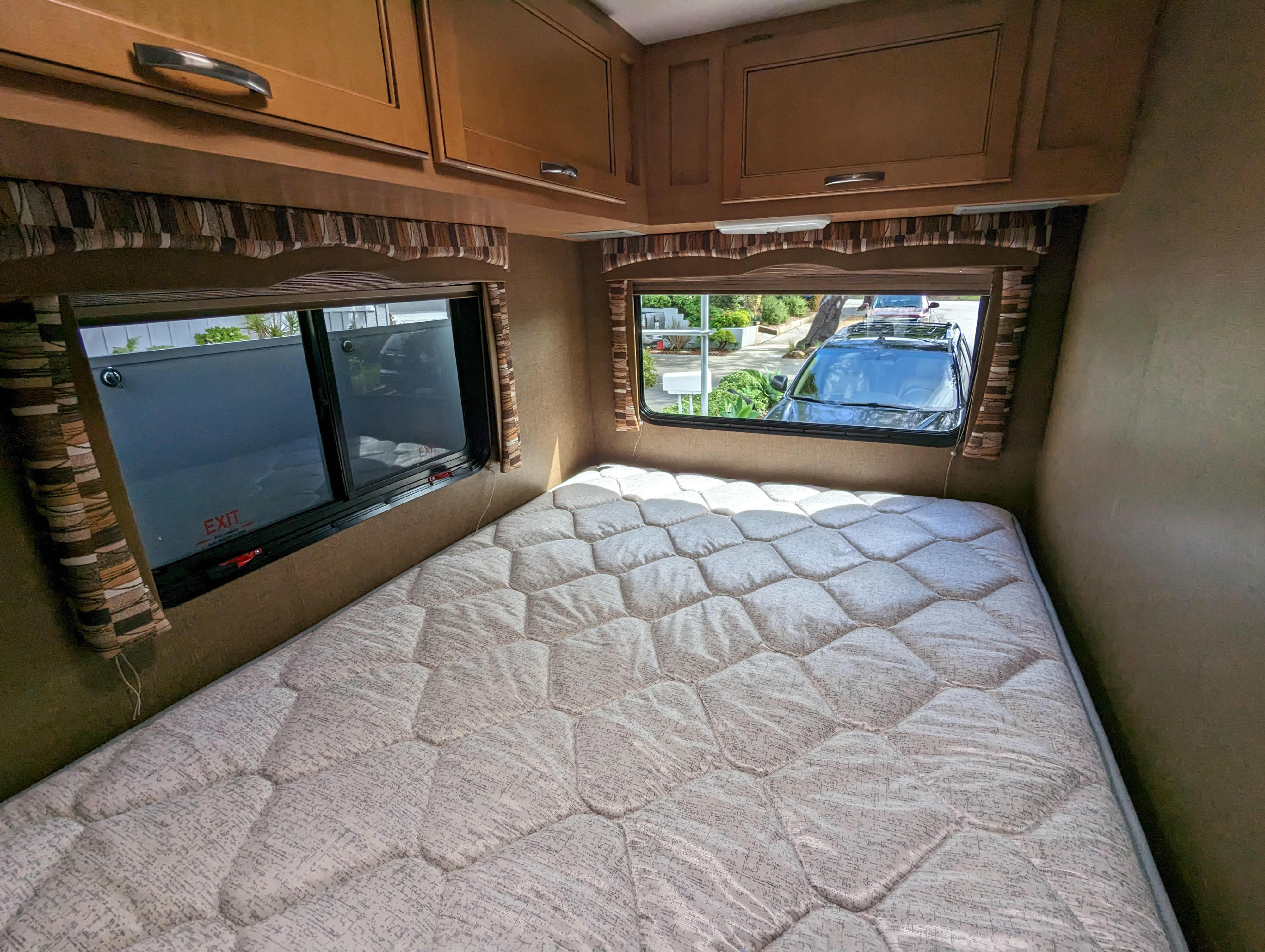 Comfortable RV rental bedroom with a quilted mattress, wooden cabinets, and windows offering views of the outdoors.. Thor Chateau 2015