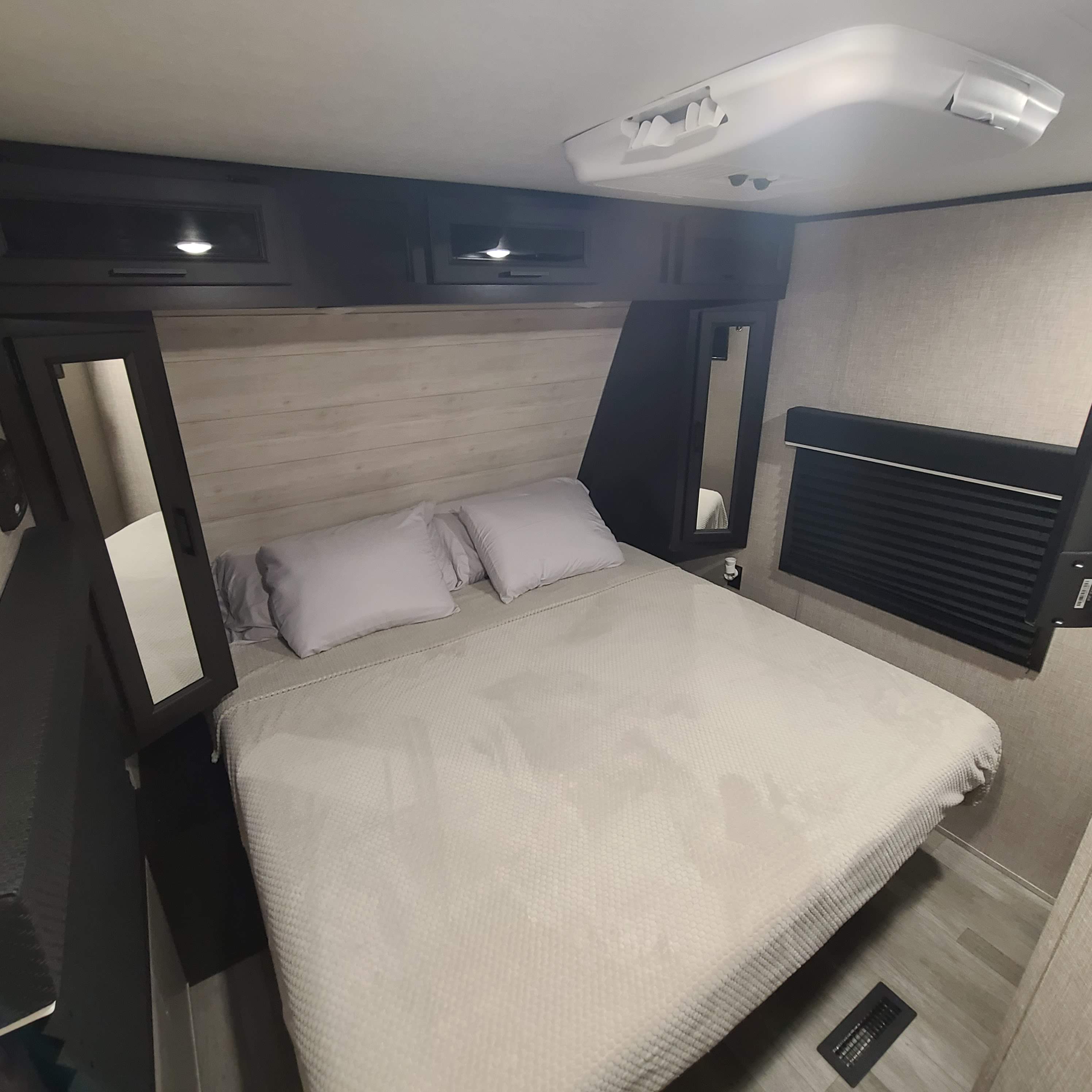 Comfortable RV rental bedroom with a large bed, overhead storage, and integrated mirrors, showcasing a compact yet functional interior.. Jayco Jay Flight 2022