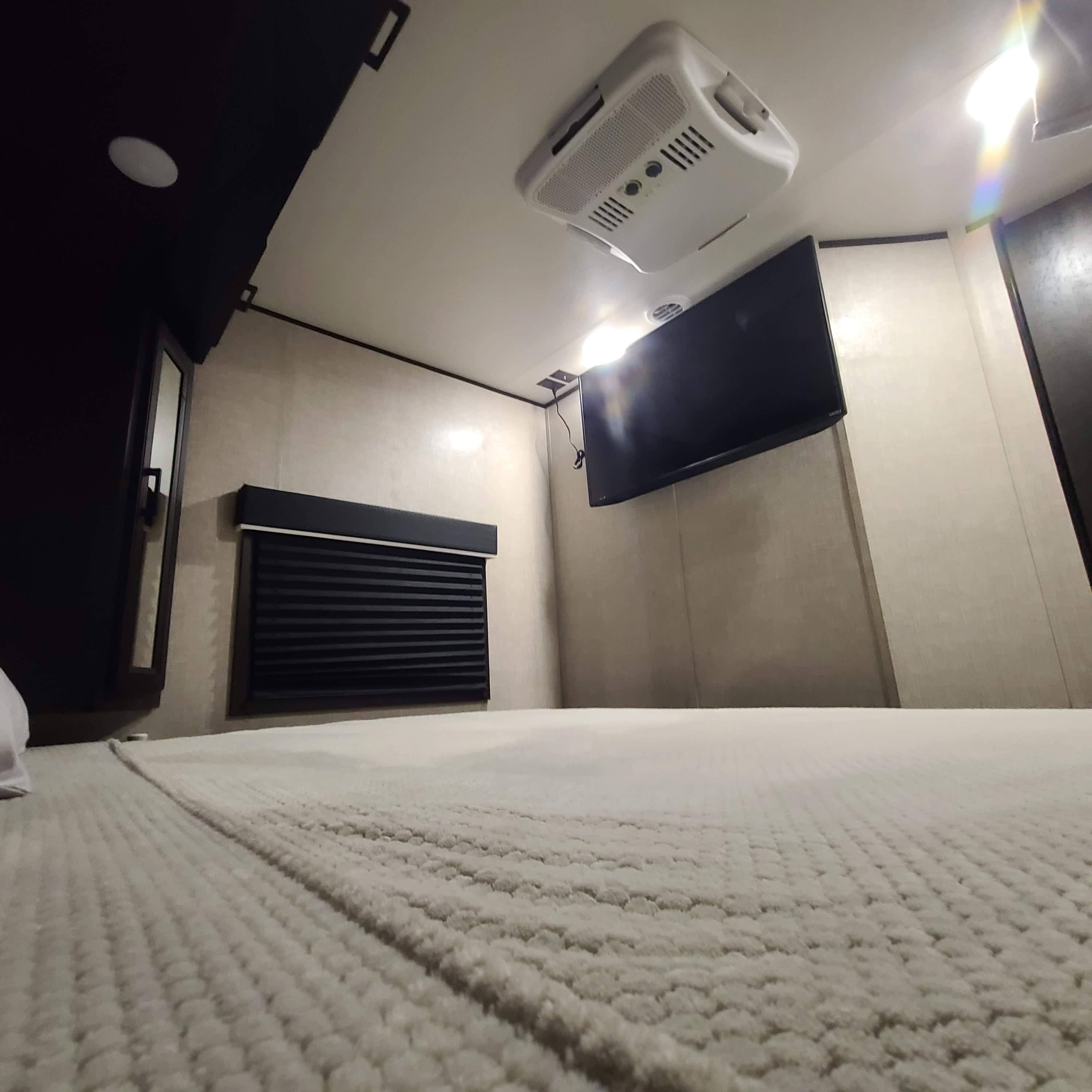 Comfortable RV rental bedroom featuring a textured bed, wall-mounted TV, and ceiling AC unit.. Jayco Jay Flight 2022