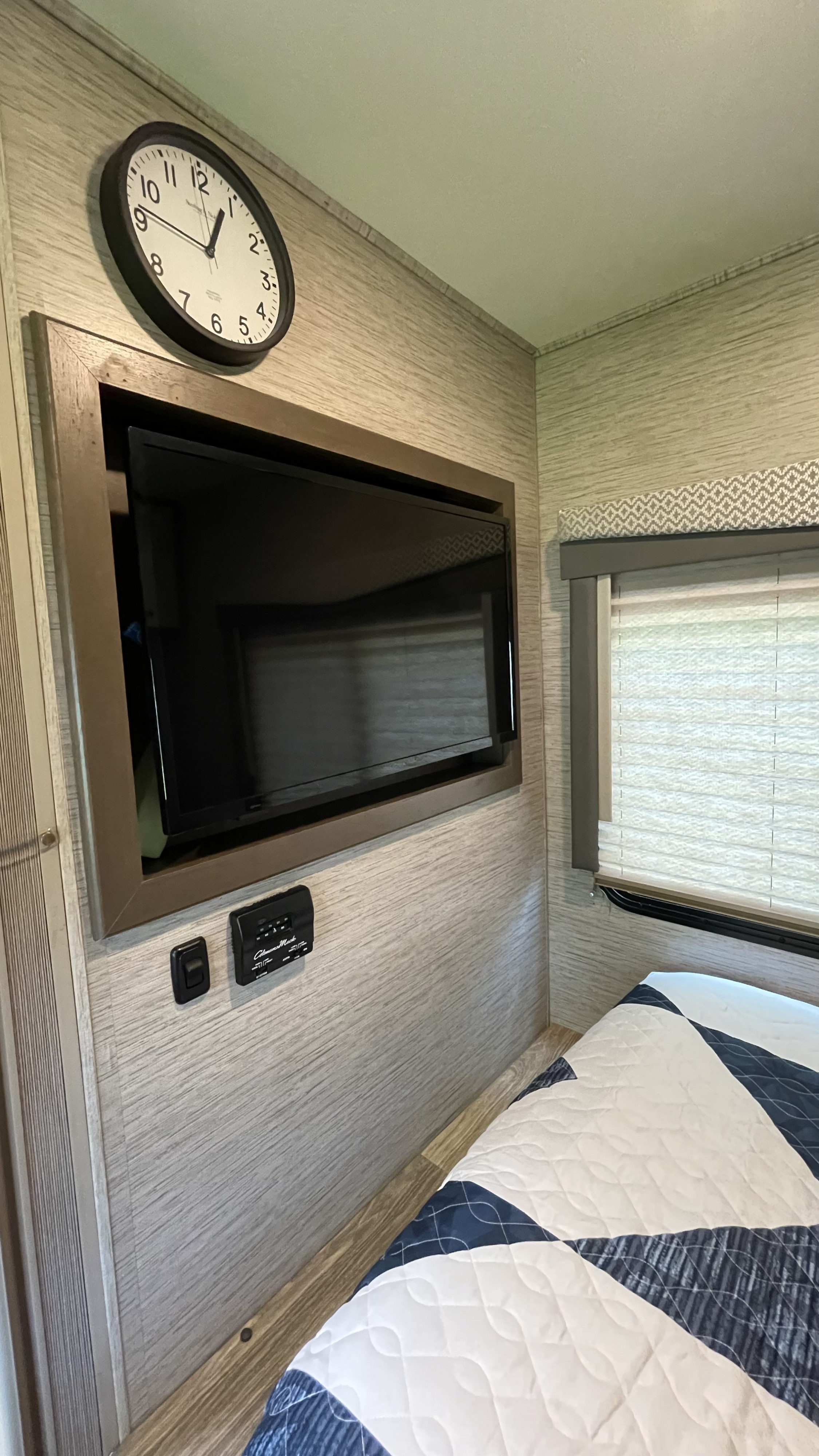 Compact RV rental bedroom featuring a wall-mounted TV, clock, and window, perfect for travelers seeking comfort.. Thor Motor Coach Four Winds 2021