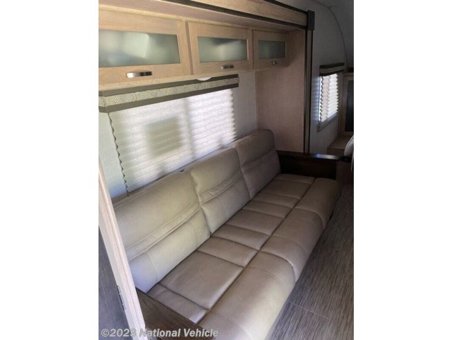 Interior of an RV rental, featuring a long, light-colored sofa, overhead cabinets, and windows with pleated blinds.. Forest River R-Pod 2020
