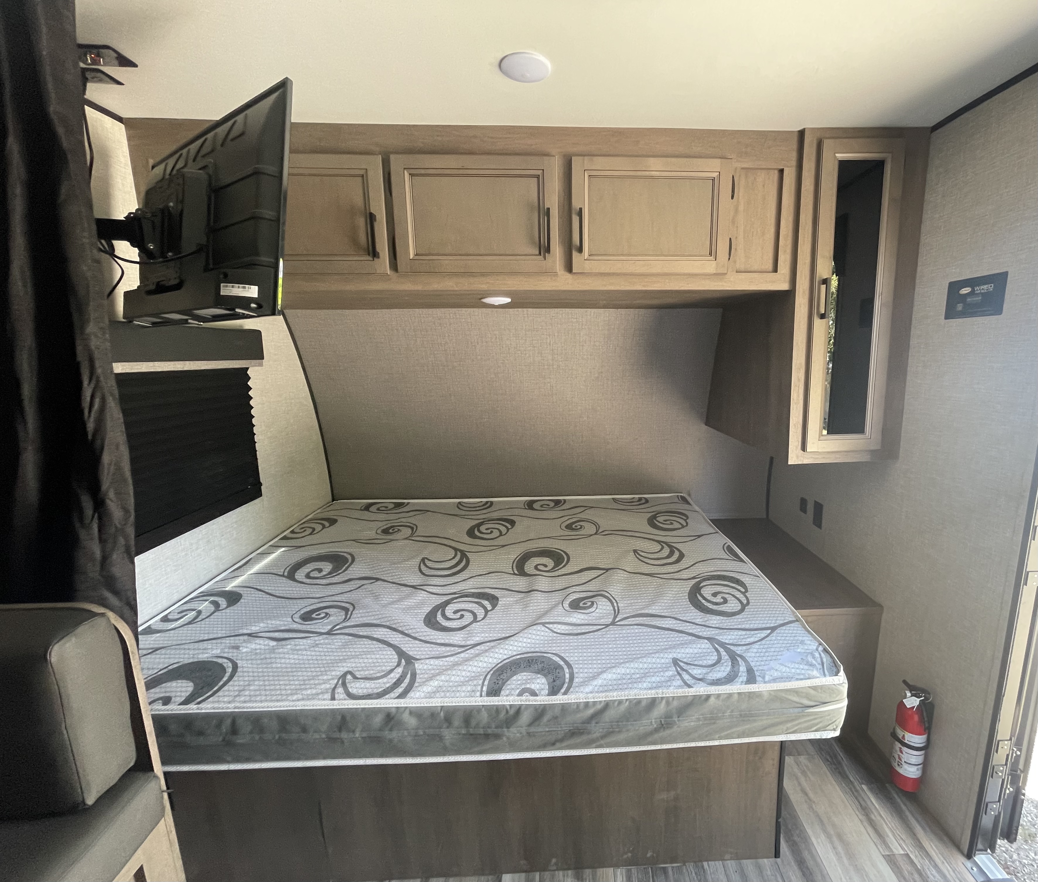 Interior of an RV rental bedroom showing a bed with a gray patterned mattress, overhead storage cabinets, and a wall-mounted TV.. Highland Ridge Open Range 2023