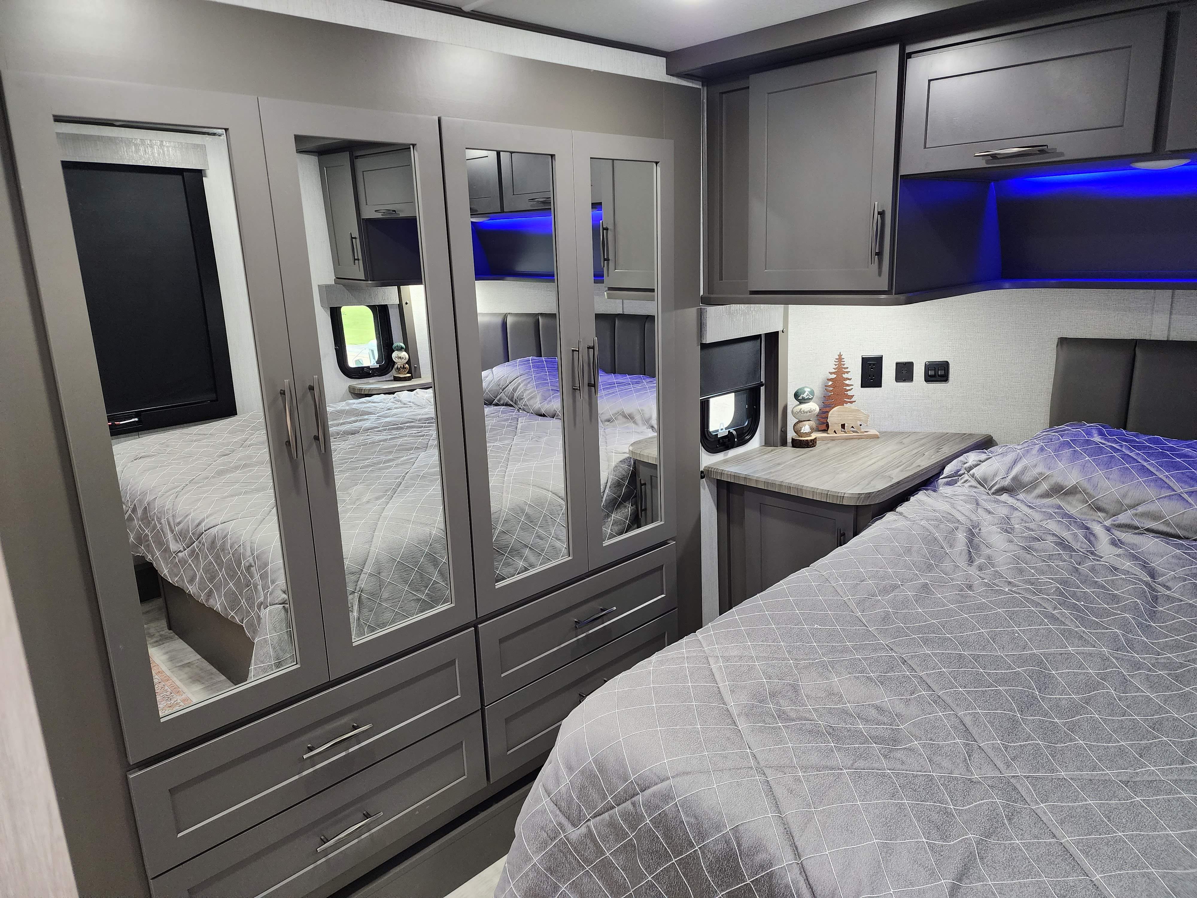 Spacious RV rental bedroom with a grey patterned bed, mirrored wardrobe, and modern overhead storage.. Grand Design Momentum 2023