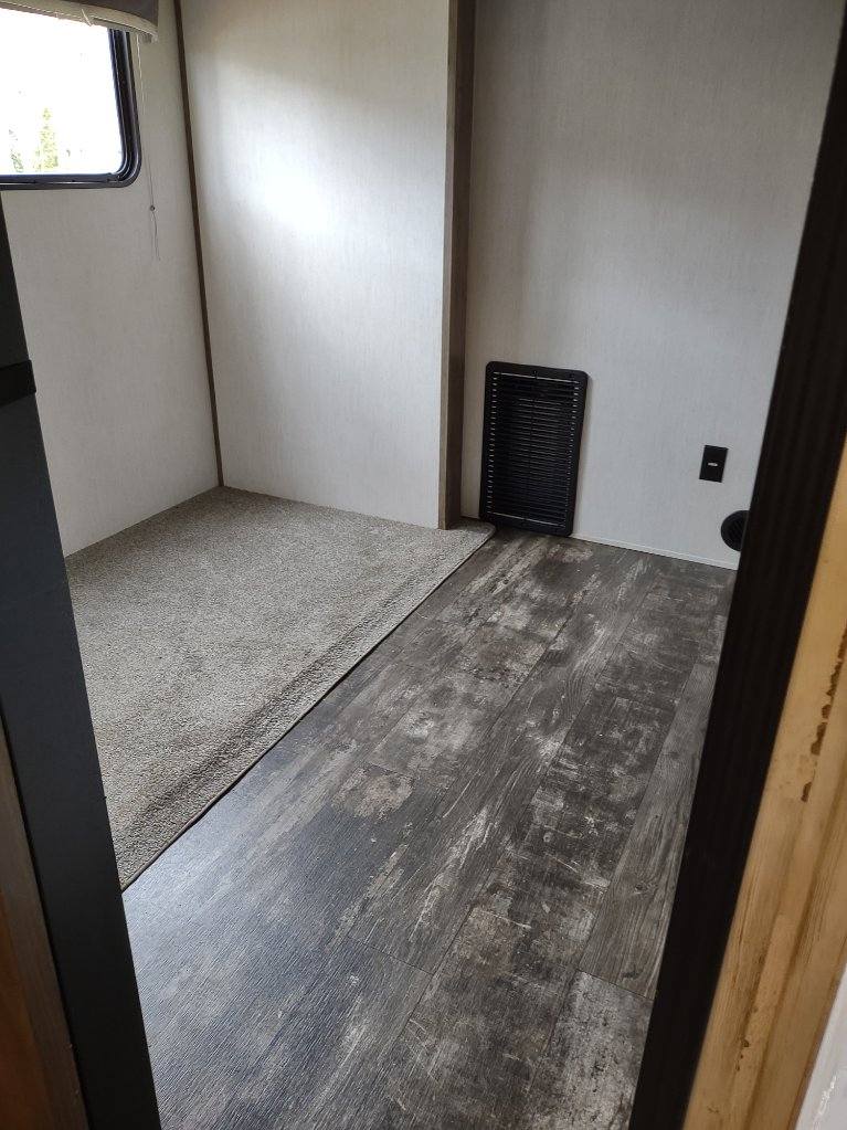 RV rental's compact interior: grey carpeted nook, dark wood-look flooring, window, and wall heater.. Forest River Sabre 2021