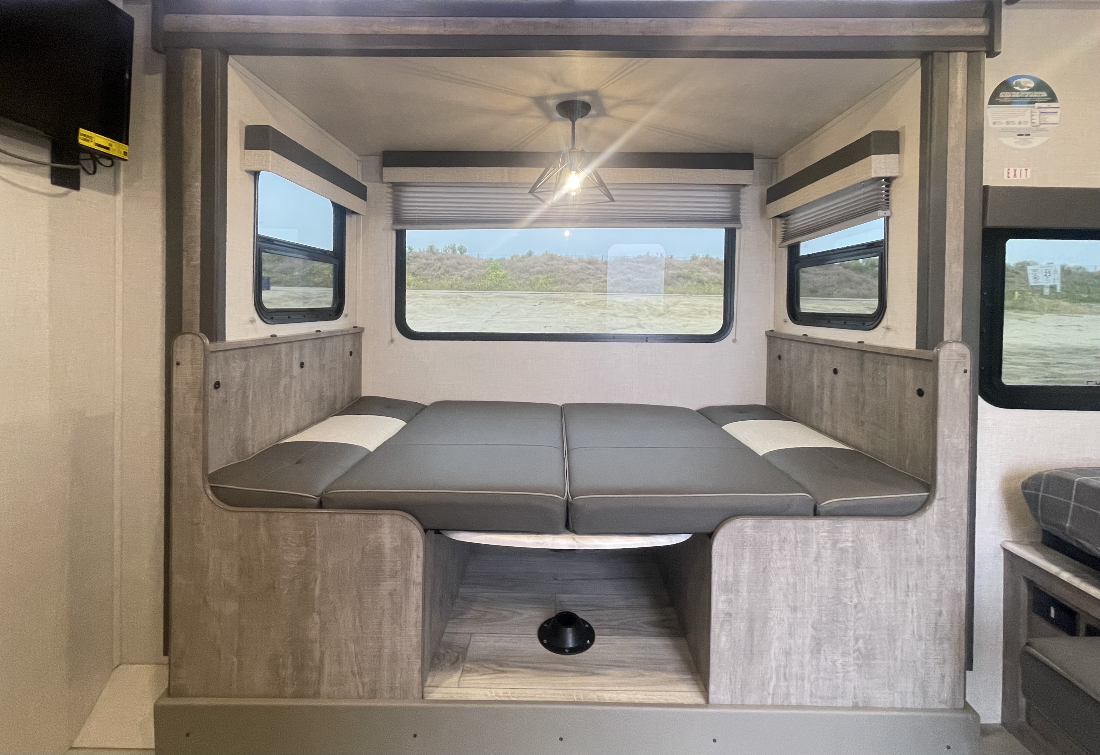 RV rental interior: A transformed dinette with grey cushions forms a spacious bed, bathed in light from large windows.. Forest River Surveyor Legend 2023