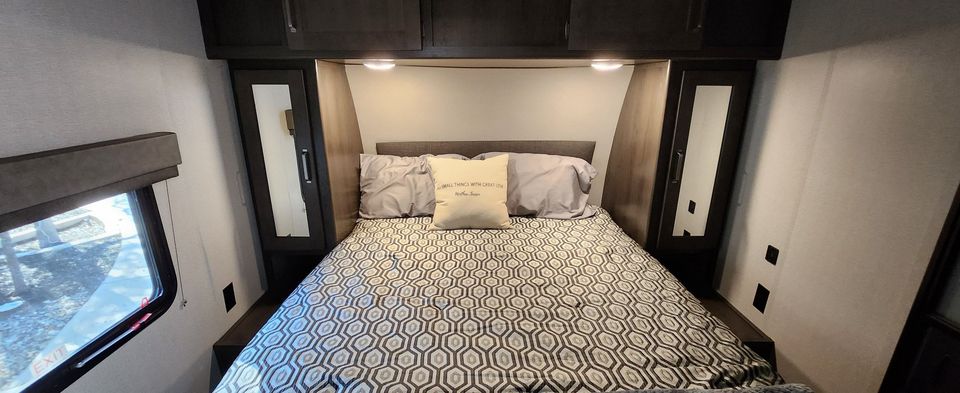 Cozy RV rental bedroom with patterned comforter, pillows, and ample storage, ready for your travels.. Grand Design Transcend 2020
