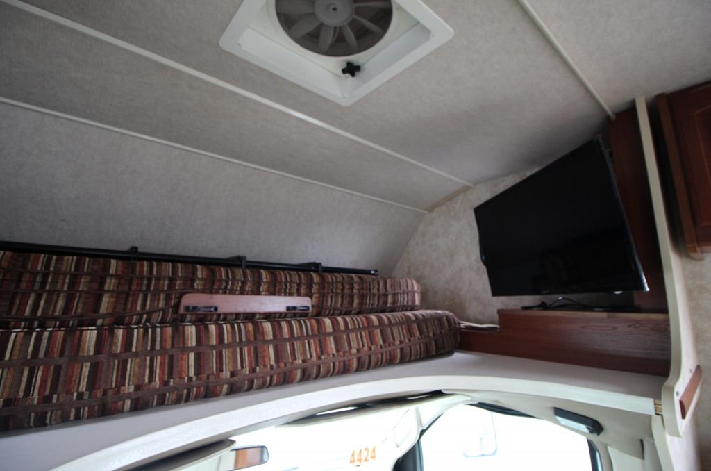 Spacious RV rental cab-over area with comfy striped cushions, wall-mounted TV, and a roof vent for air circulation.. Winnebago Access 2011