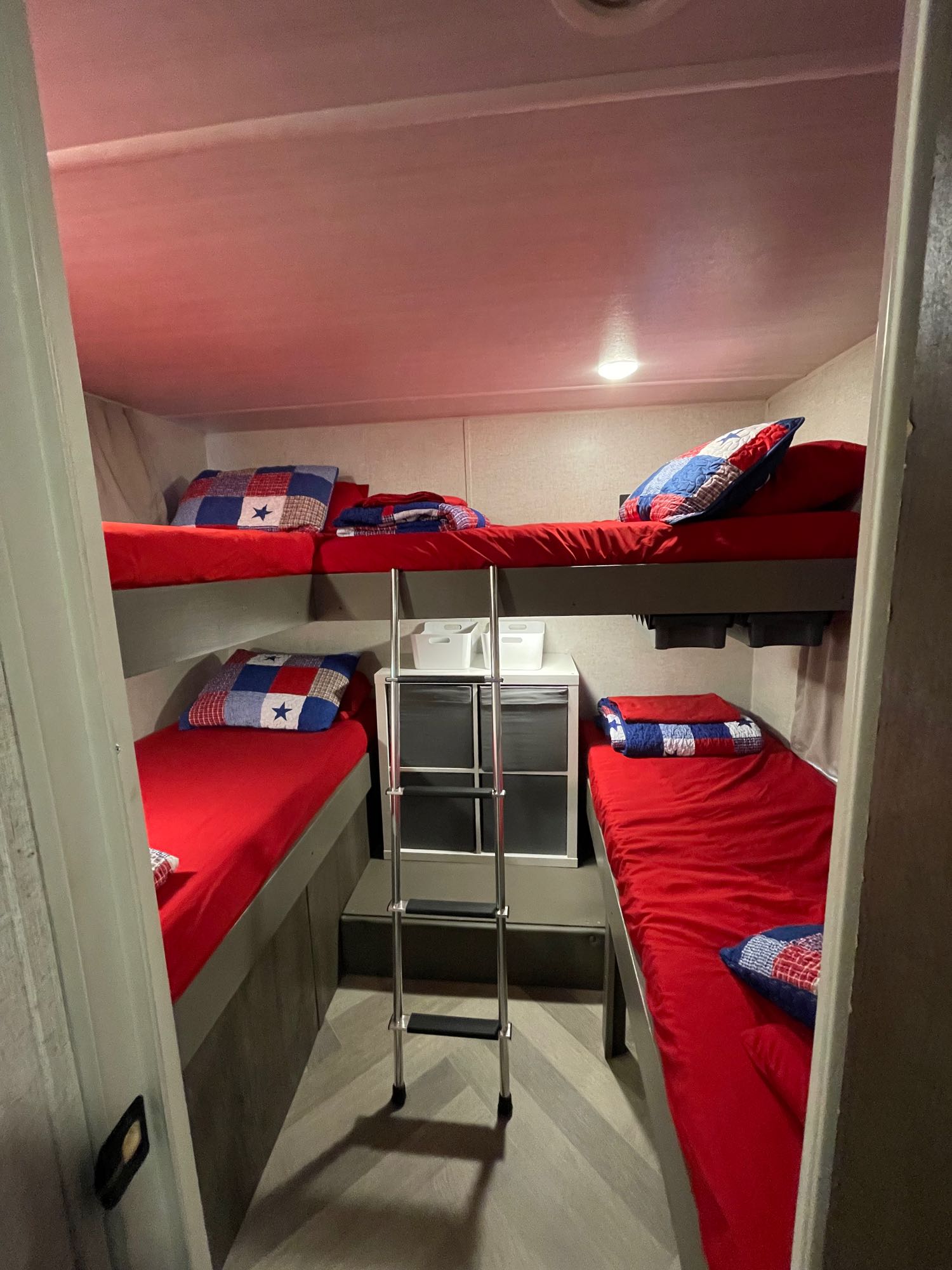 Cozy RV rental bunk beds with bright red bedding & patriotic pillows, providing compact sleeping for an adventure.. Forest River Wildwood X-Lite 2020