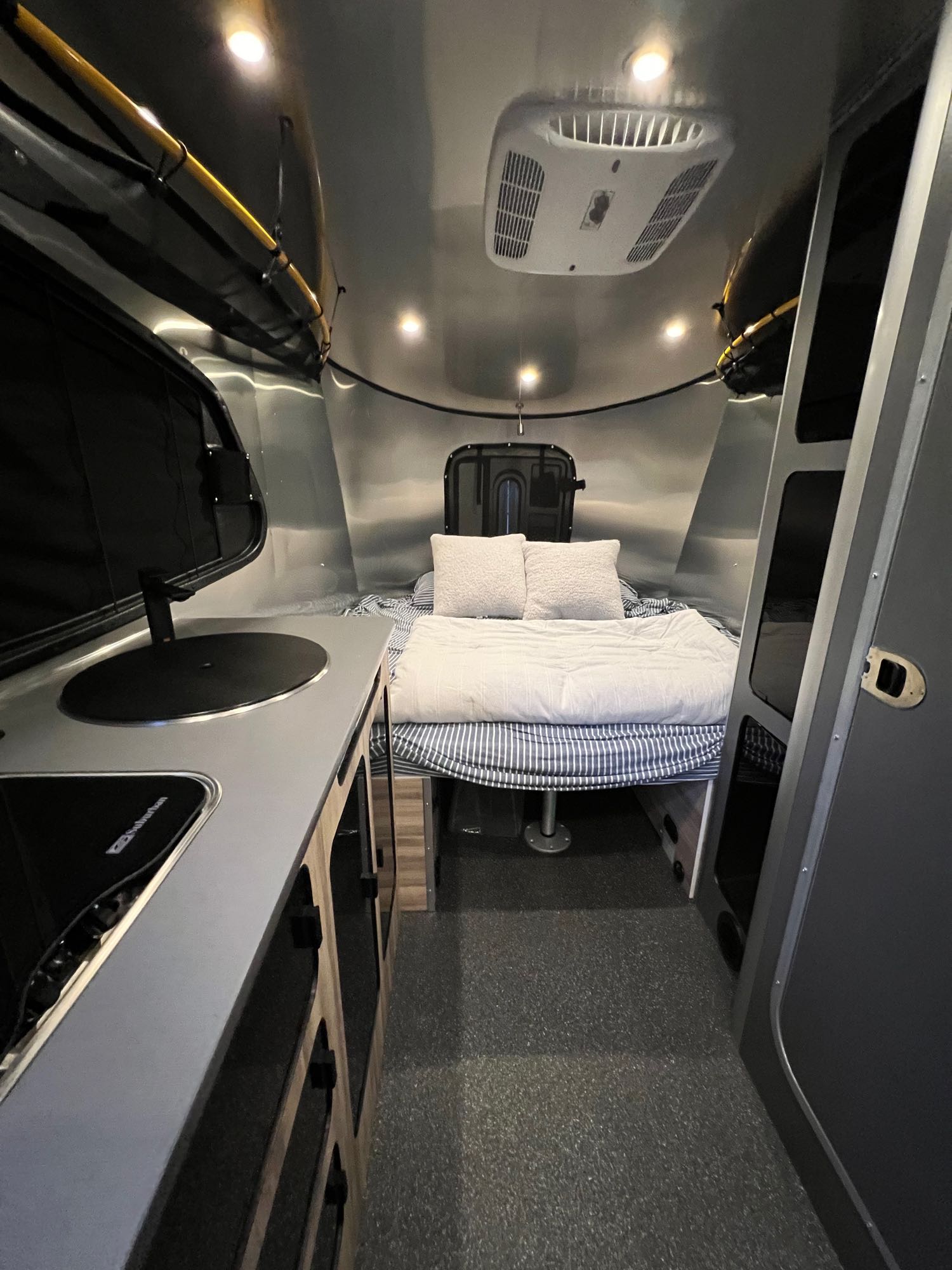 Inside a sleek RV rental, showcasing a built-in kitchen, cozy bed area, and overhead AC unit for comfortable travel.. Airstream Basecamp 2023