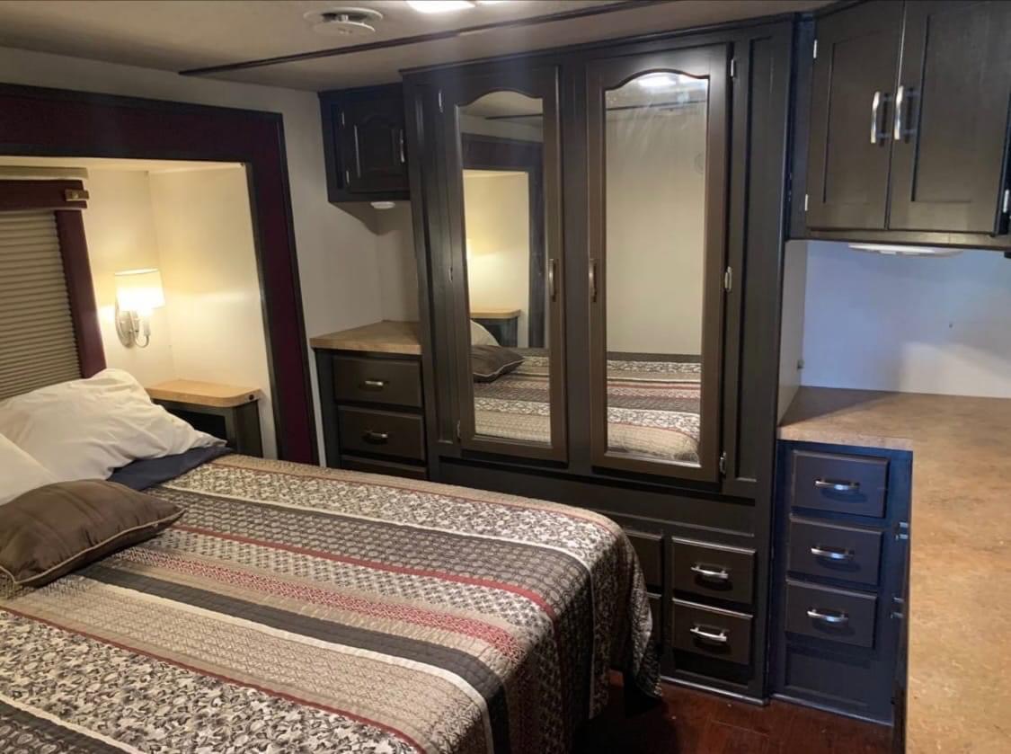 Inside an RV rental bedroom: a bed with patterned quilt, dark built-in cabinets, mirrored wardrobe, and side tables with lamps.. Damon Intruder 1999