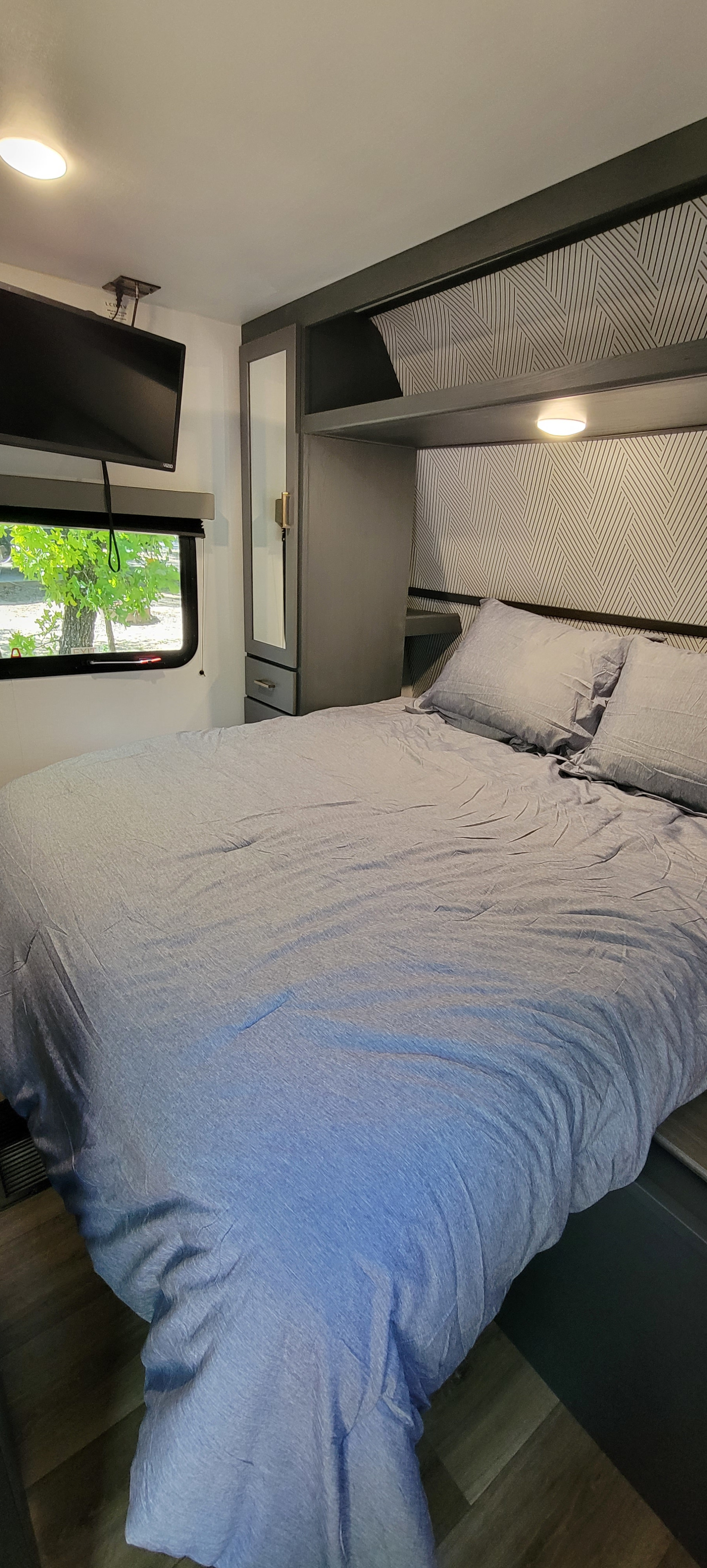 Modern RV rental bedroom featuring a comfy bed, overhead storage, TV, and large window.. Keystone RV Bullet Crossfire 2022
