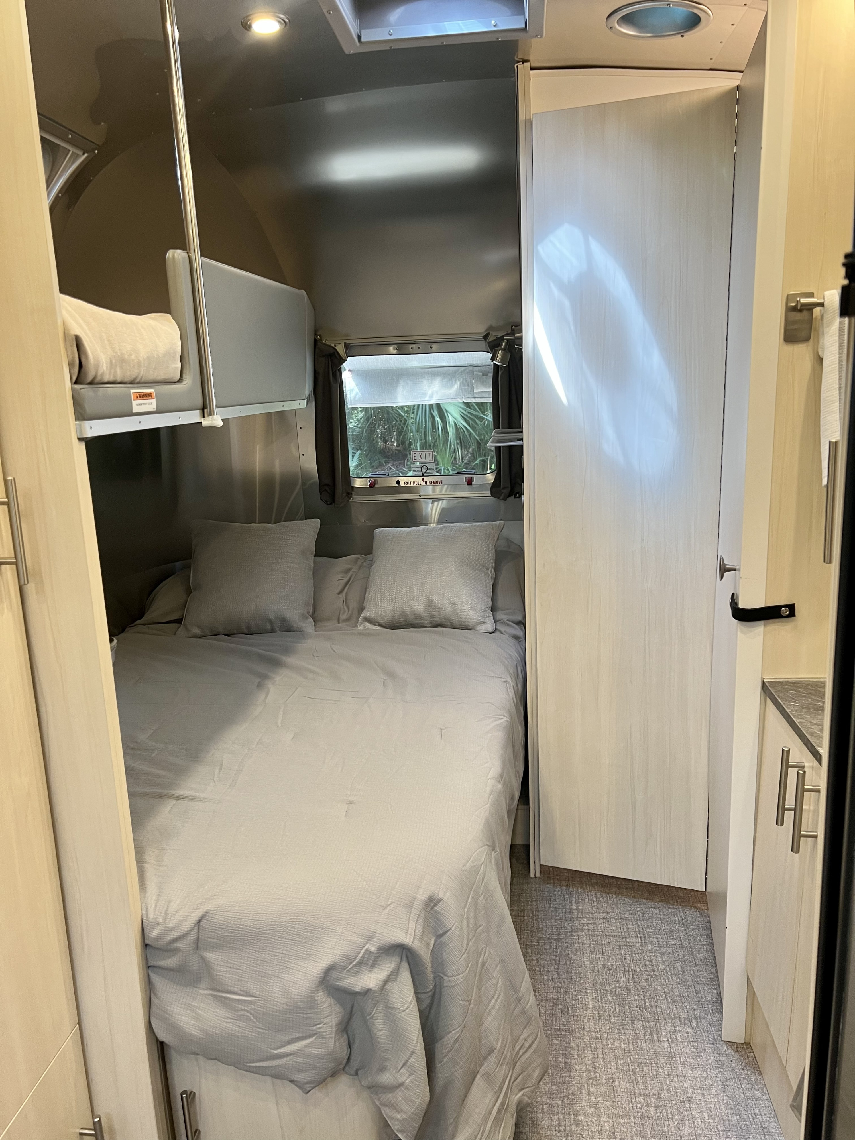Cozy RV rental bedroom with a main bed, upper bunk, metallic walls, window view, and wood-toned cabinets.. Airstream Flying Cloud 2021