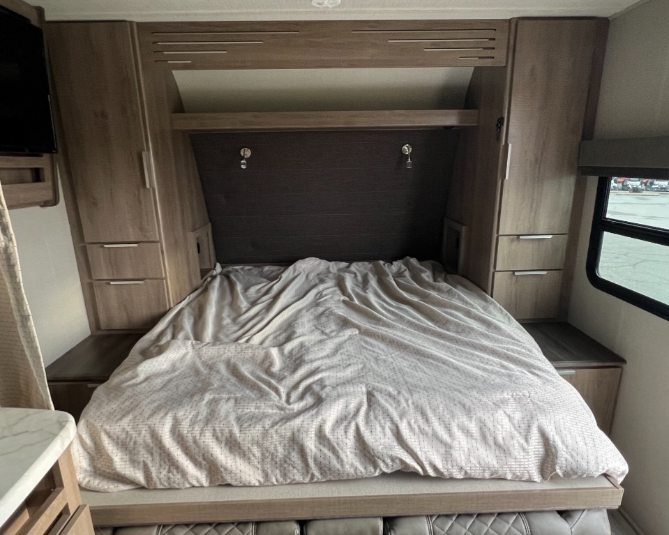 RV rental interior: A cozy bedroom with a rumpled bed, built-in storage, and a window for natural light.. Grand Design Imagine XLS 2021
