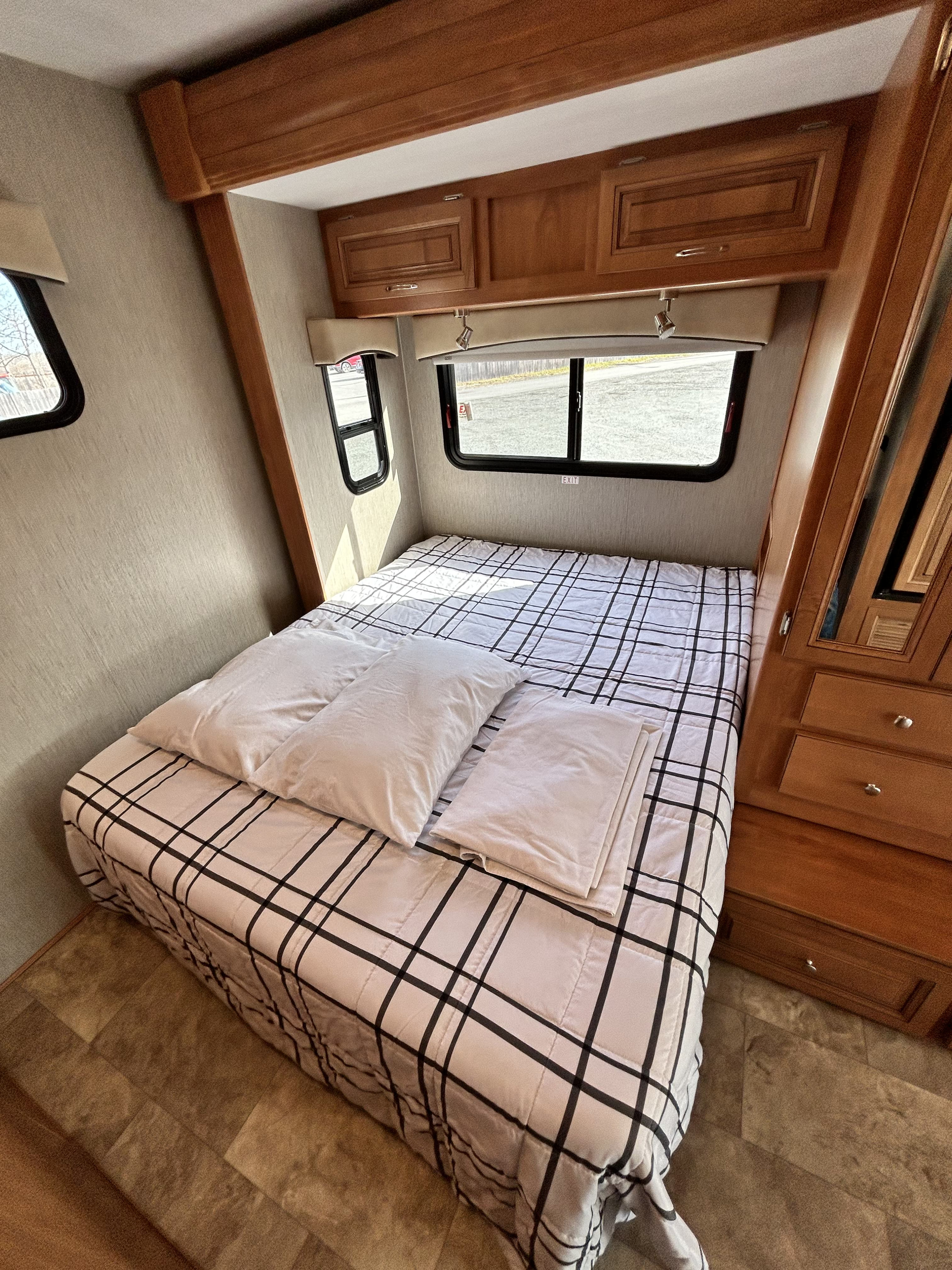 Spacious RV rental bedroom with a comfy bed, plaid comforter, wood cabinets, and bright windows.. Nexus Phantom 2019