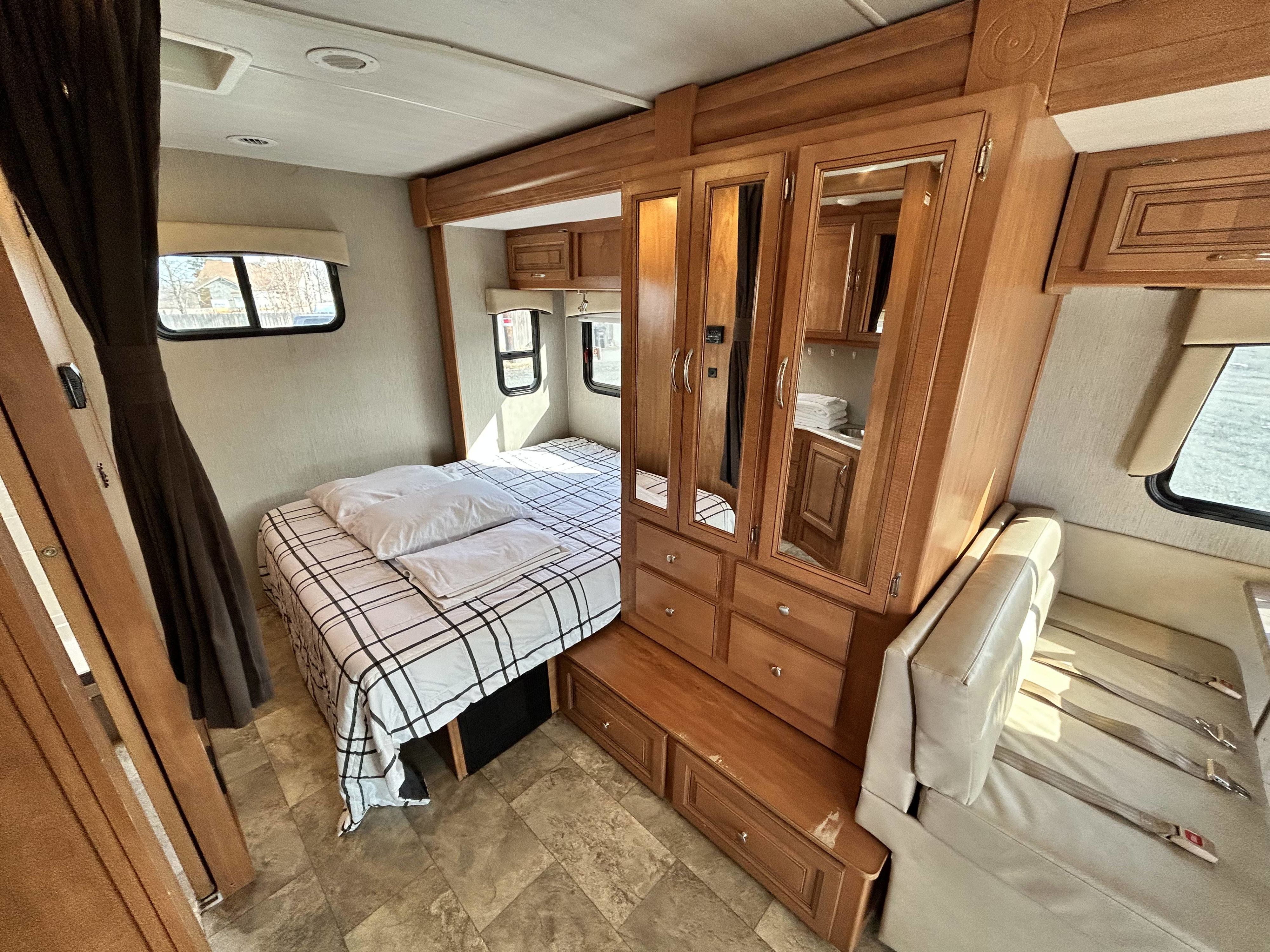 Comfortable RV rental interior: view of the compact bedroom with plaid bedding and bright living area with bench seat.. Nexus Phantom 2019