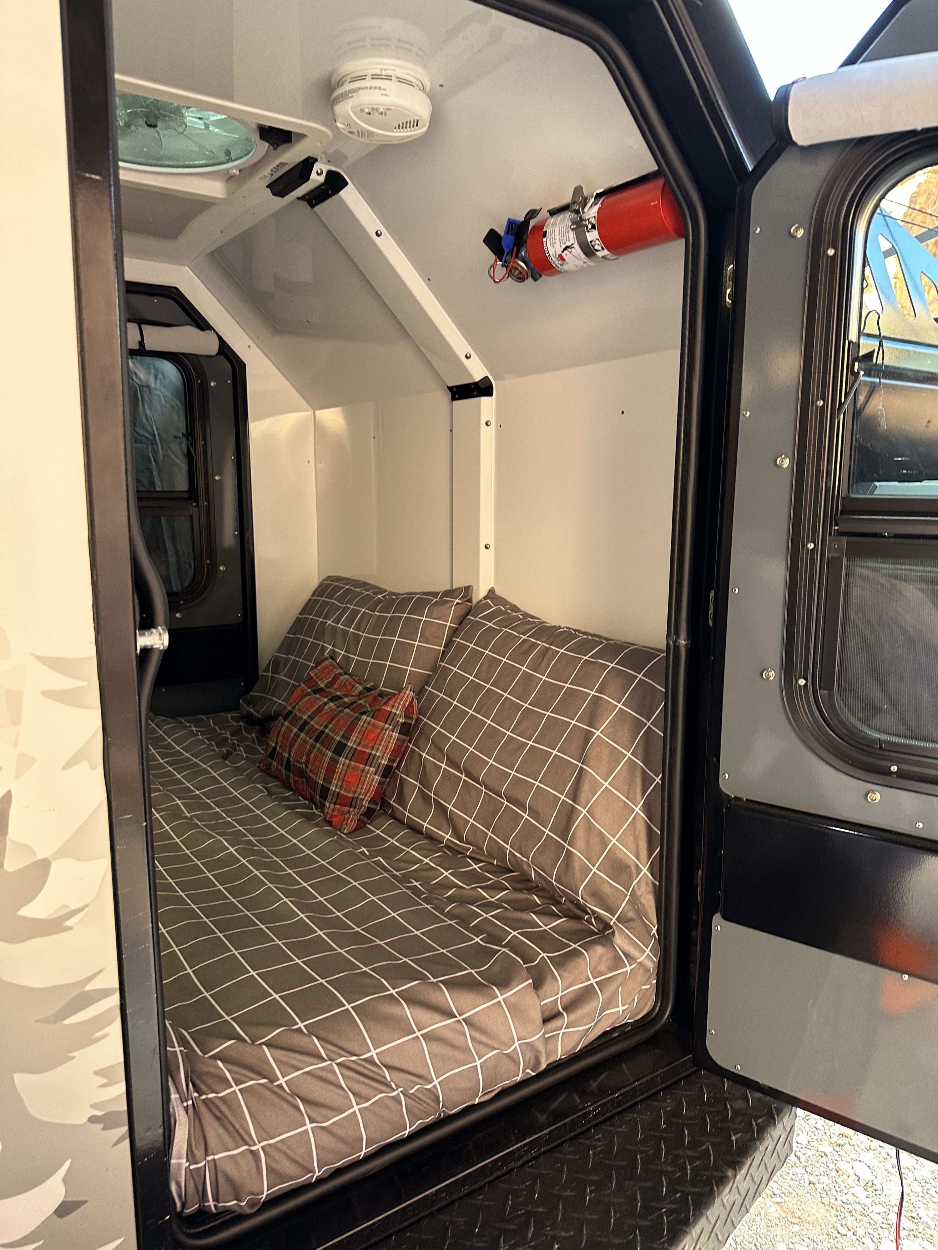 Cozy compact **RV rental** interior with a bed, fan, and safety features like a smoke detector and fire extinguisher.. Off Grid Trailers Off Grid Trailers Trailer 2022