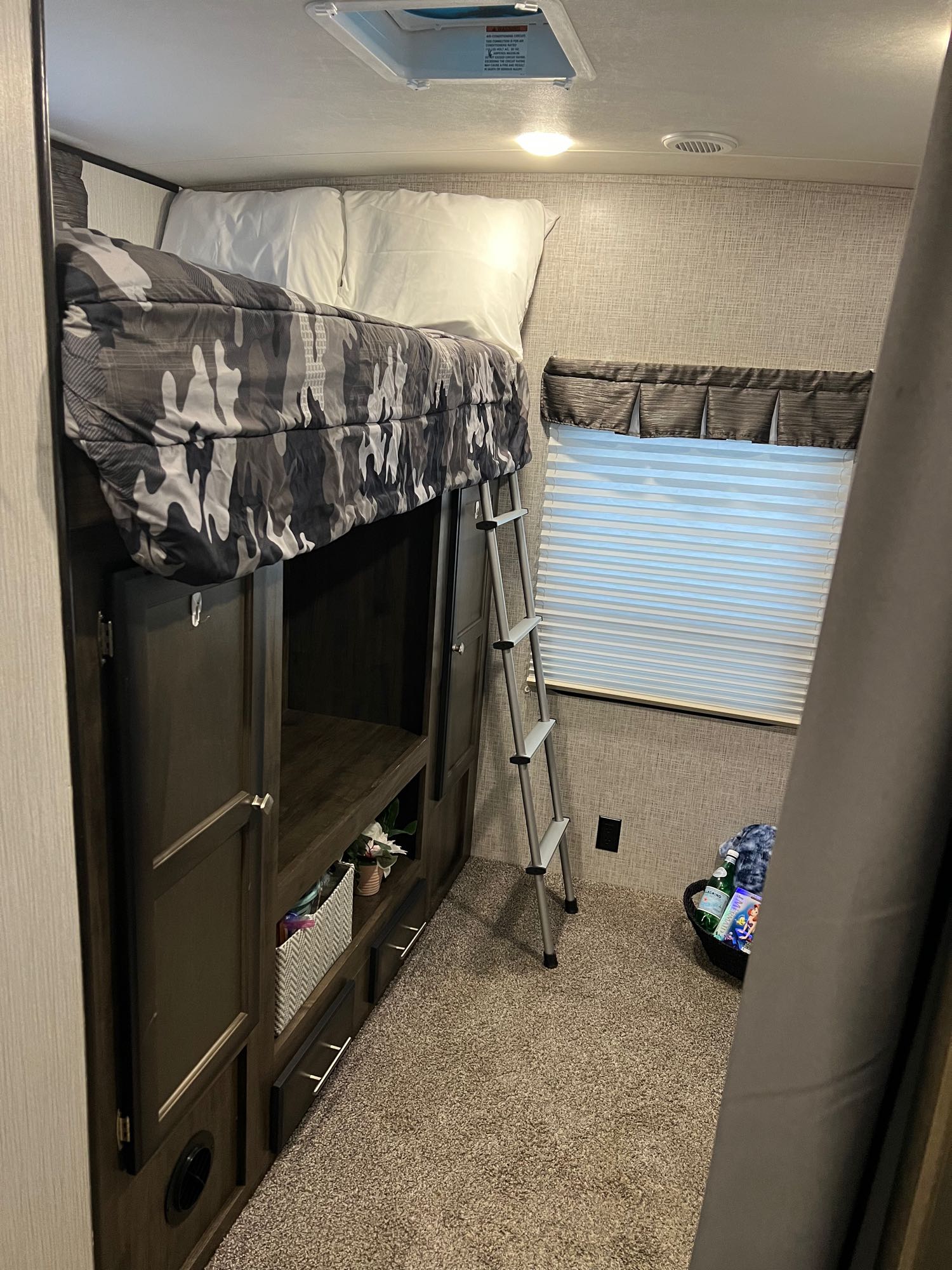 This cozy RV rental bunk area features a bed with camouflage bedding, built-in storage, and a ladder.. Heartland RVs Mallard 2020