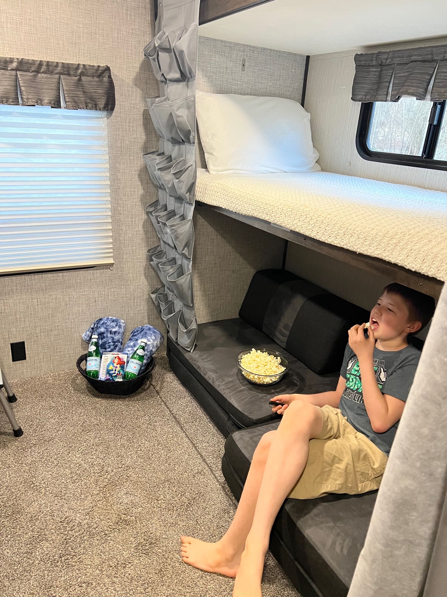 Cozy rv rental bunk bed area for kids' movie night. A child enjoys popcorn while watching a movie. Basket with treats and blankets.. Heartland RVs Mallard 2020