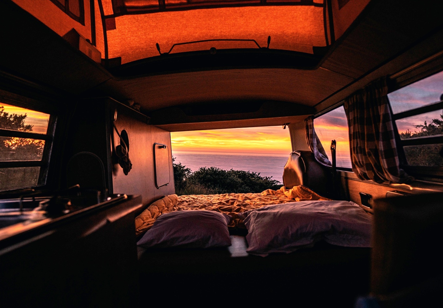 Cozy RV rental interior with bed facing a stunning ocean sunset. Ideal for your next van life adventure!. Volkswagen T2 Westfalia 1971