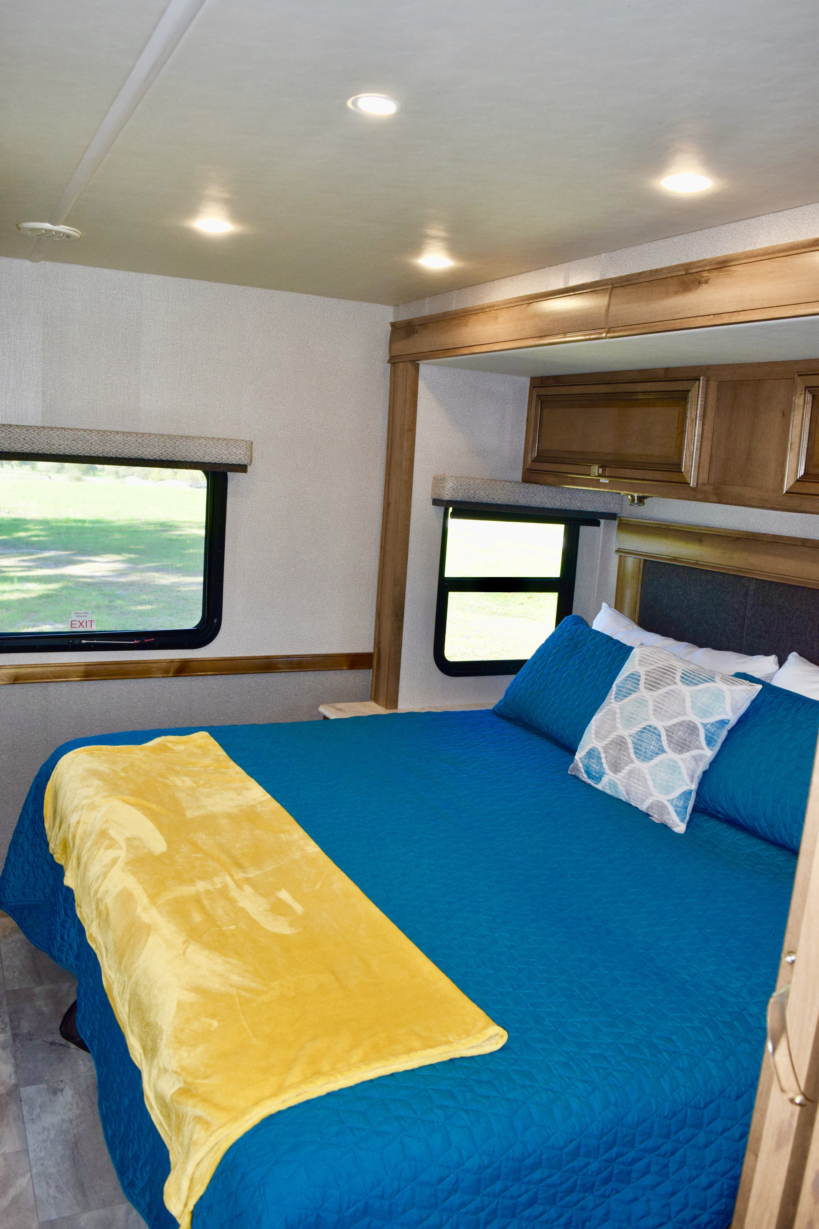RV rental bedroom: blue bed, yellow blanket, pillows, windows, and wood accents, perfect for a cozy travel experience.. Holiday Rambler Admiral 2021