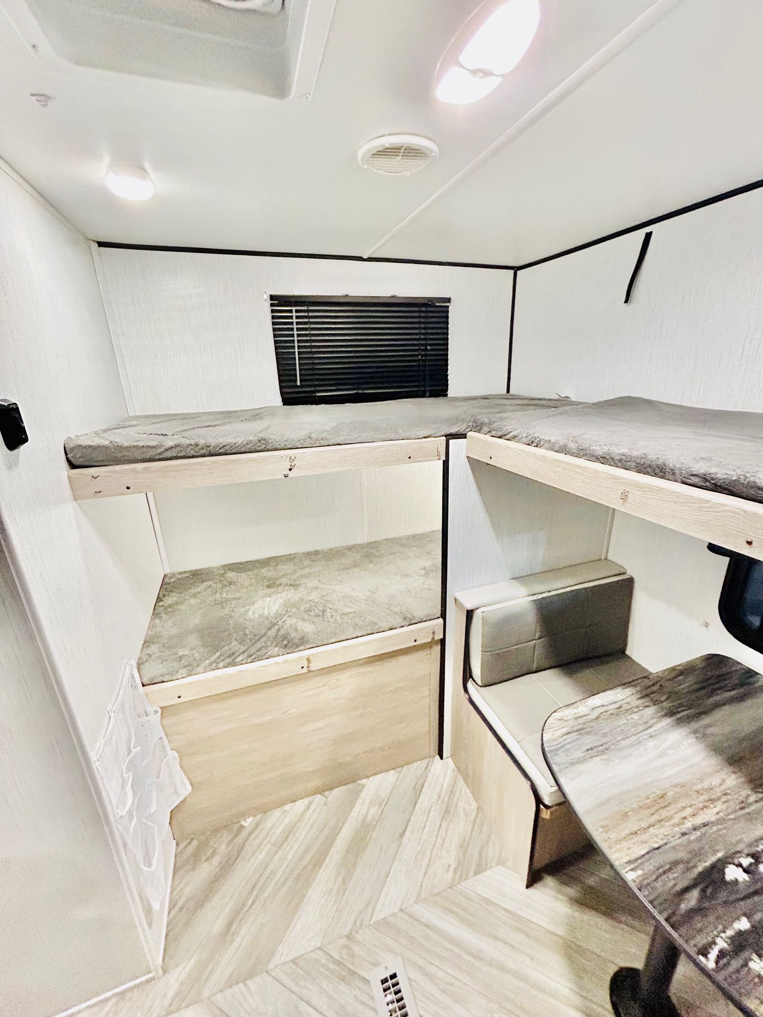 Bright rv rental interior featuring light wood-look bunk beds & a dinette with grey cushions & marble-look table.. Heartland 303BH 2022