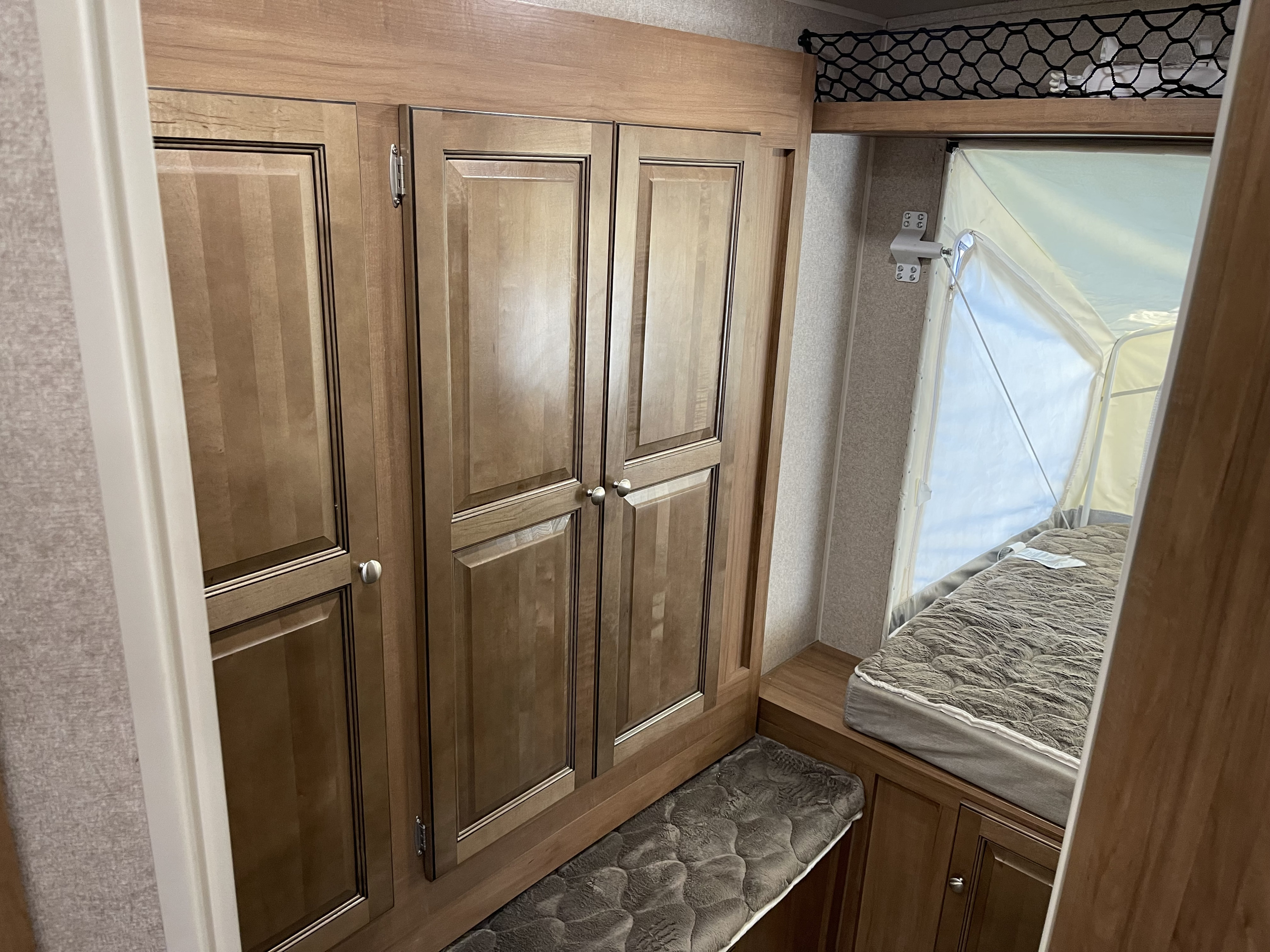 Cozy RV rental interior featuring a spacious wardrobe, pop-out bed, and overhead storage net, perfect for adventurers.. Forest River Rockwood Roo 2019