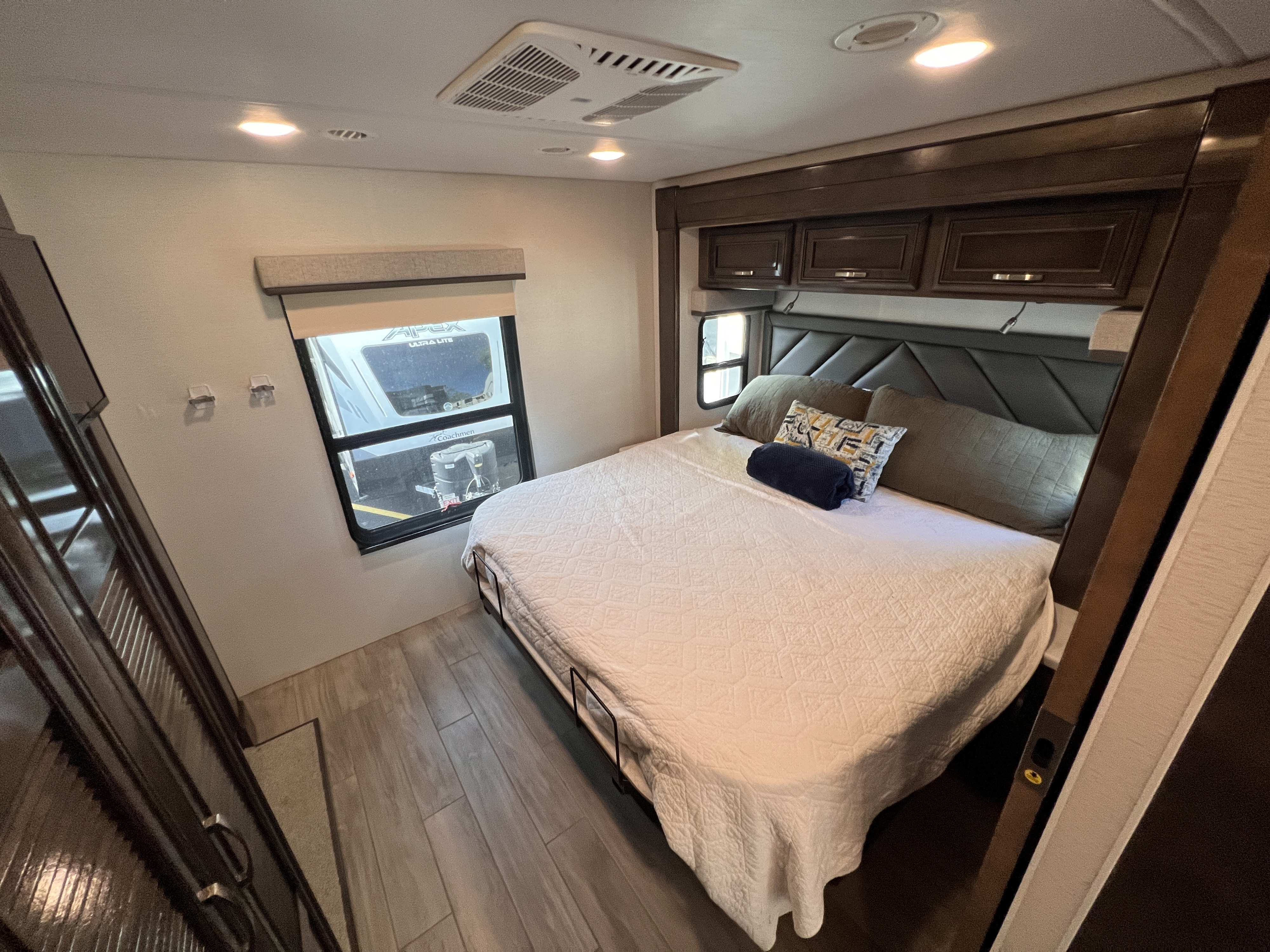Cozy RV rental bedroom with comfortable bed, overhead cabinets, and window views showing other RVs.. Entegra Coach Accolade XL 37L  Super-C 2023