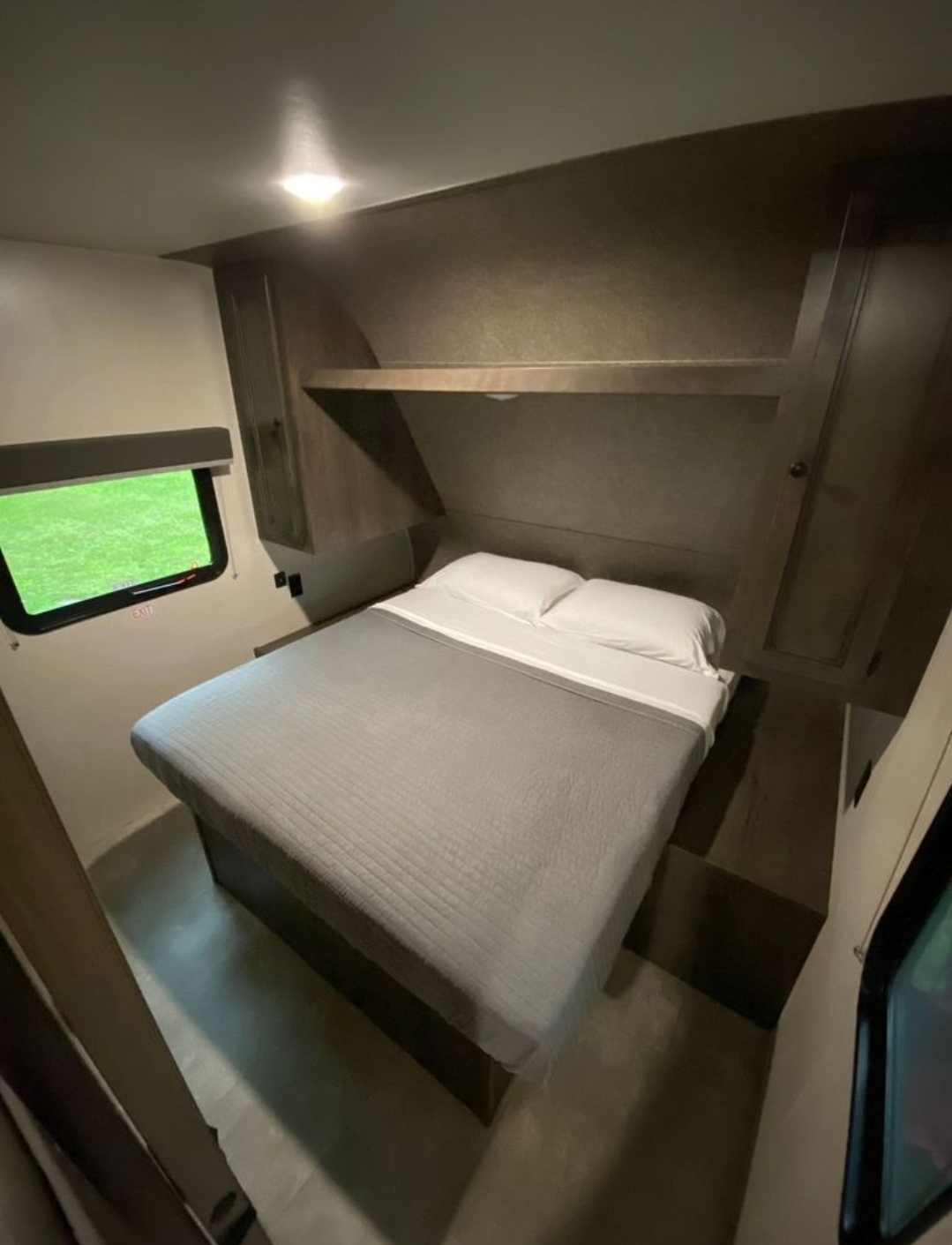 Inside an RV rental: a compact bedroom featuring a bed, overhead storage, and window with an "EXIT" sign.. Starcraft Autumn Ridge 2021